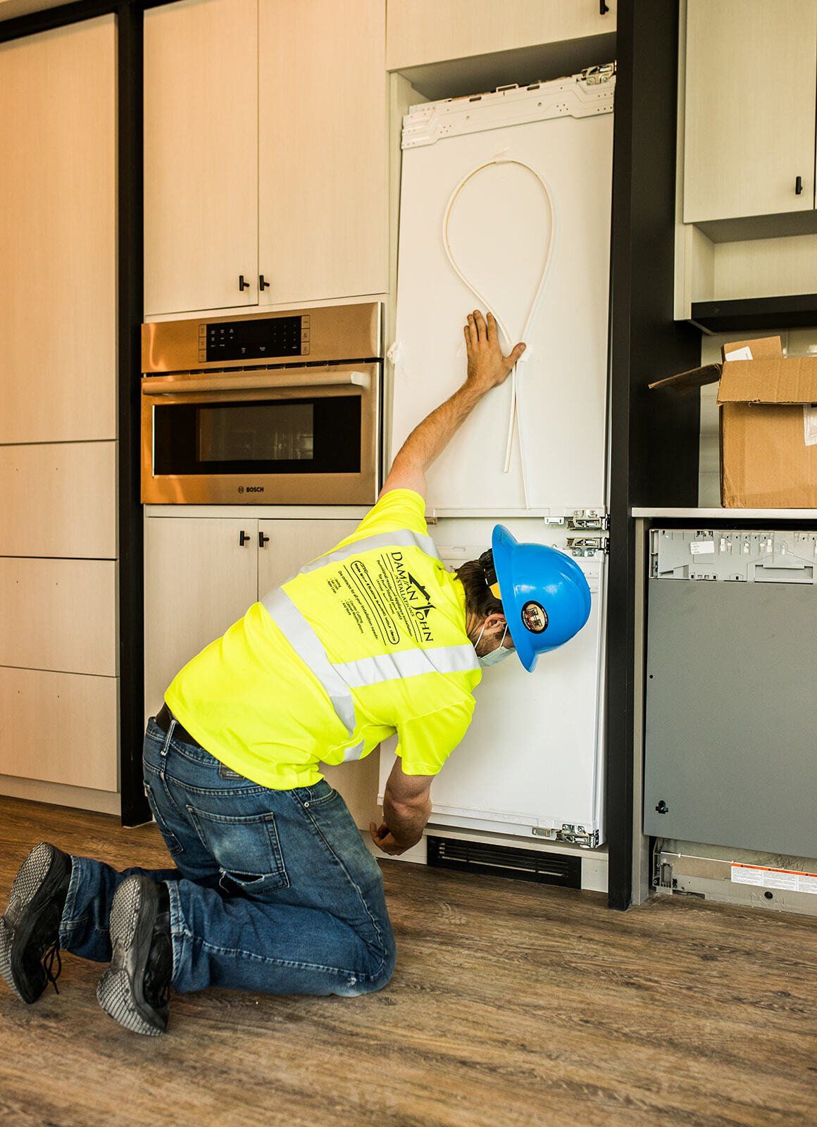 A man is kneeling down in front of a refrigerator in a kitchen.