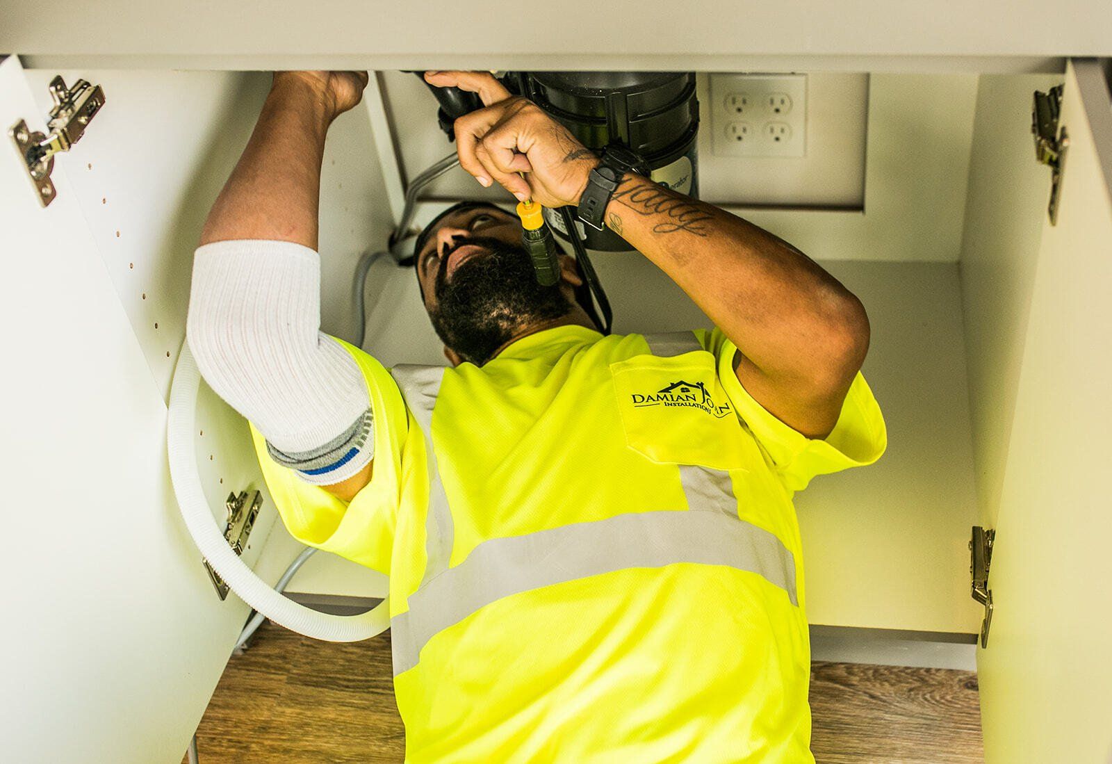 A man in a yellow shirt is working under a sink.