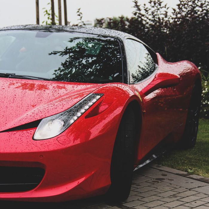 Red sports car parked on a driveway, wet with raindrops, viewed from the front-left side.