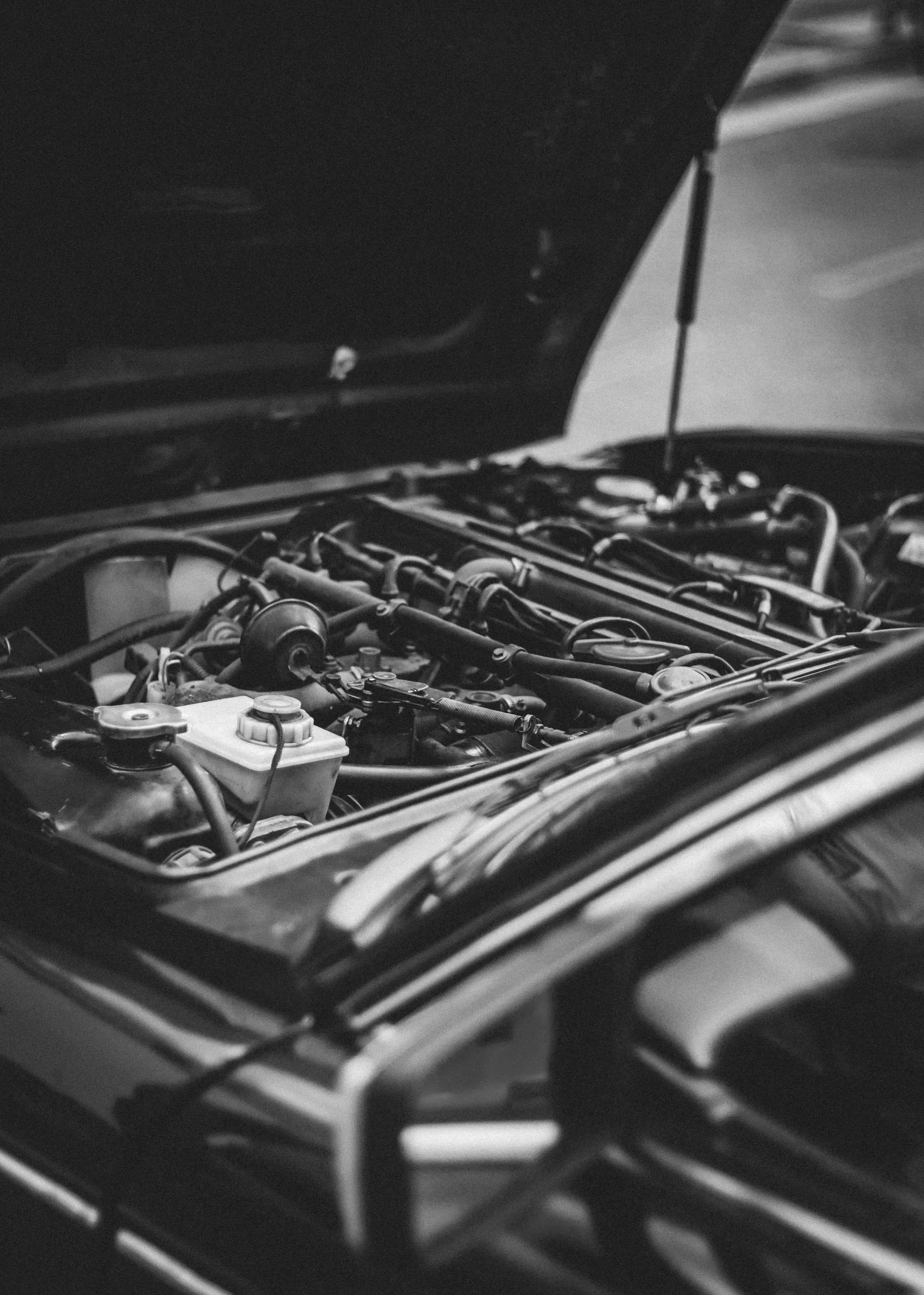 Black-and-white photo of a car engine bay with the hood open and exposed mechanical parts