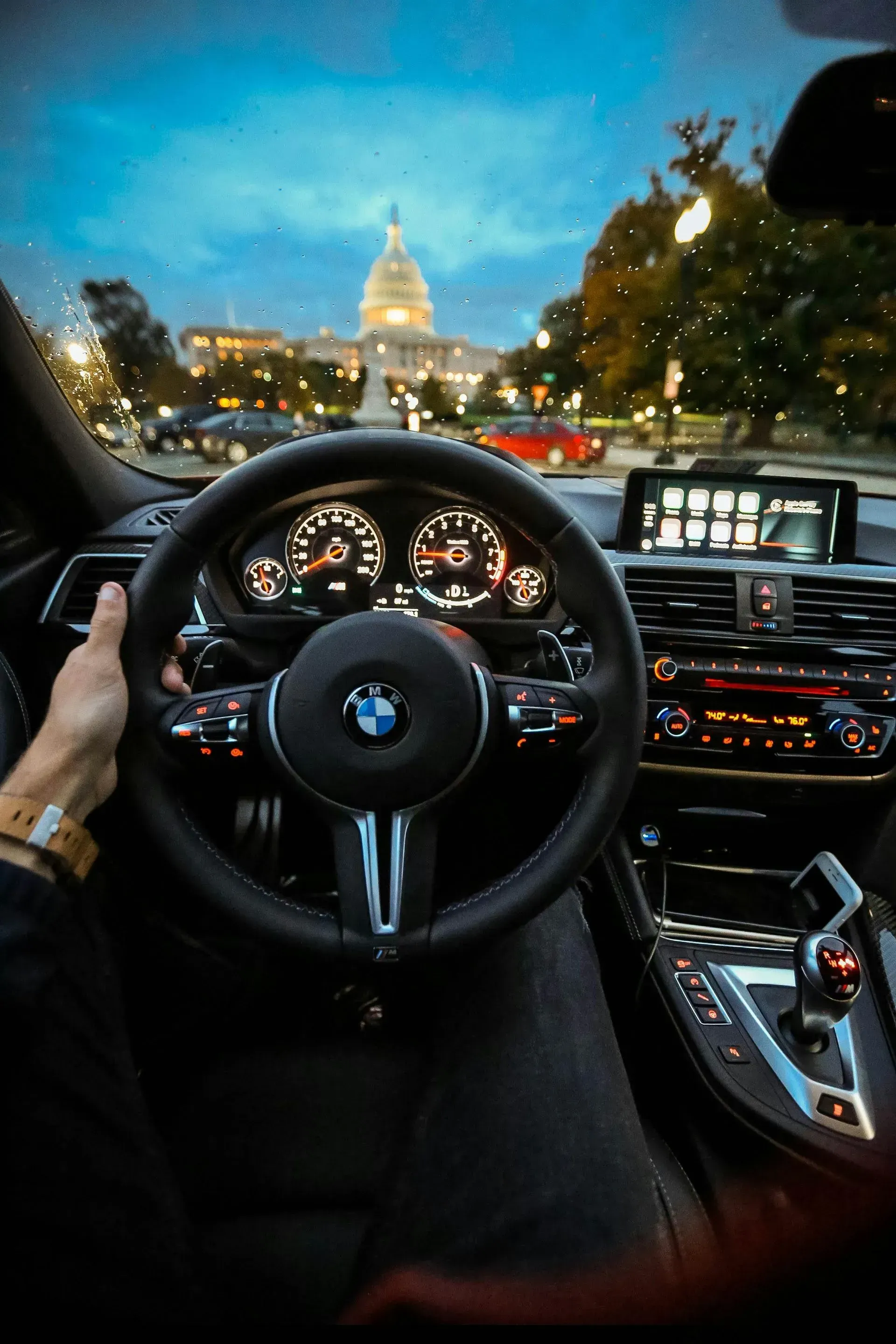BMW steering wheel view with city skyline ahead at dusk, dashboard lights glowing inside the car