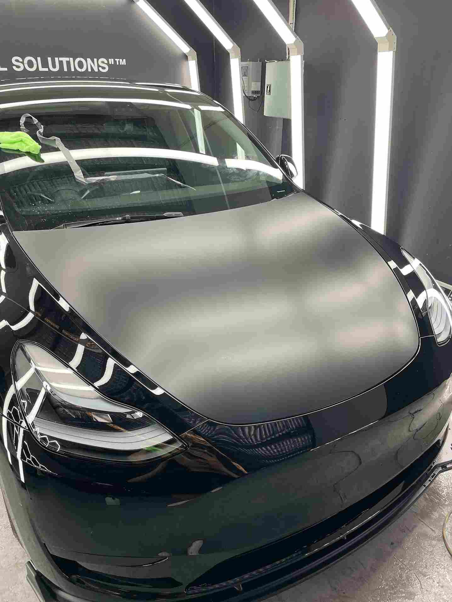 Black Tesla Model Y with matte black hood in a well-lit detailing bay.