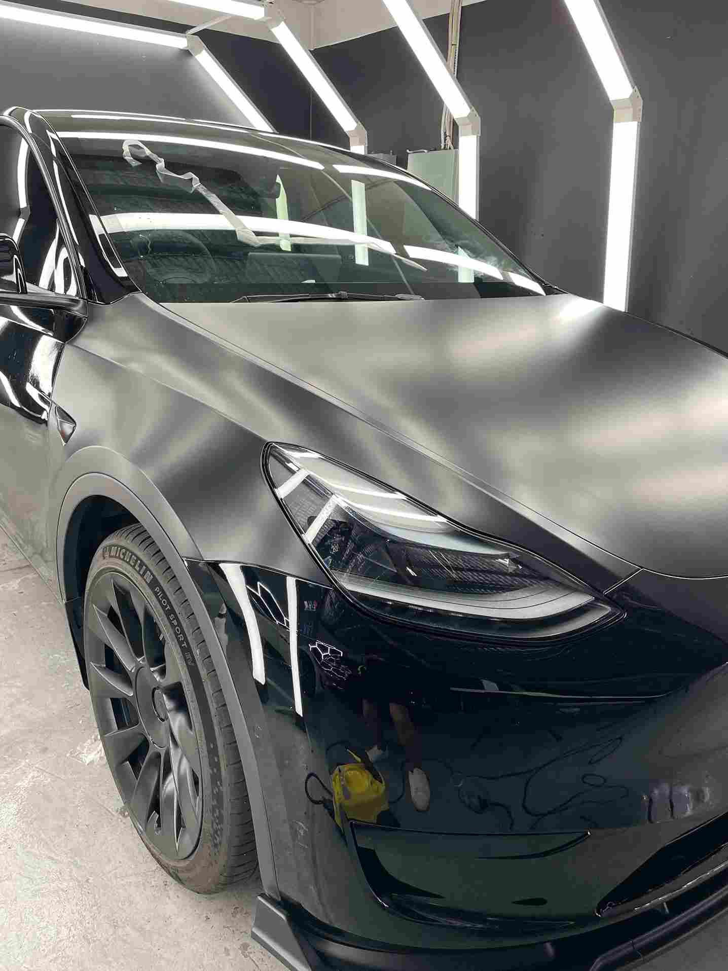 Black Tesla Model Y with matte finish, under bright lights in a shop.