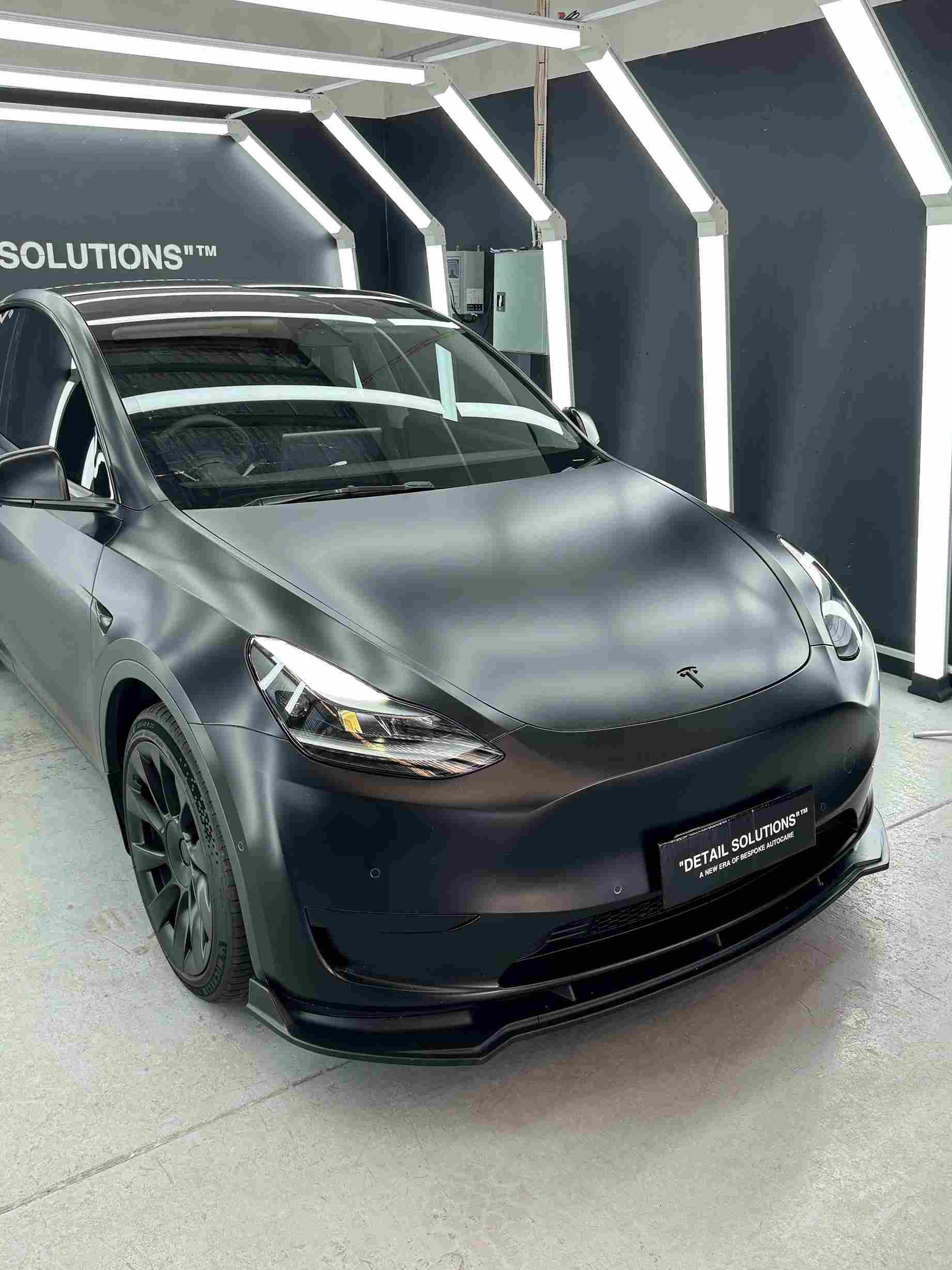 Matte black Tesla Model Y car in a brightly lit garage.