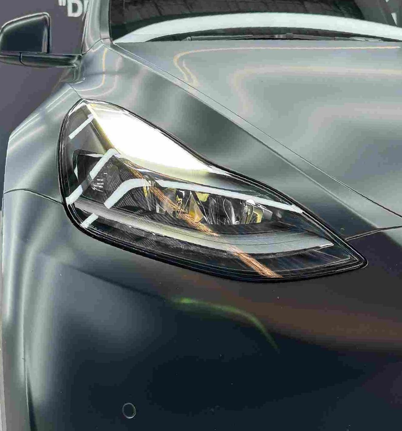Headlight and hood detail of a dark-colored Tesla Model Y.