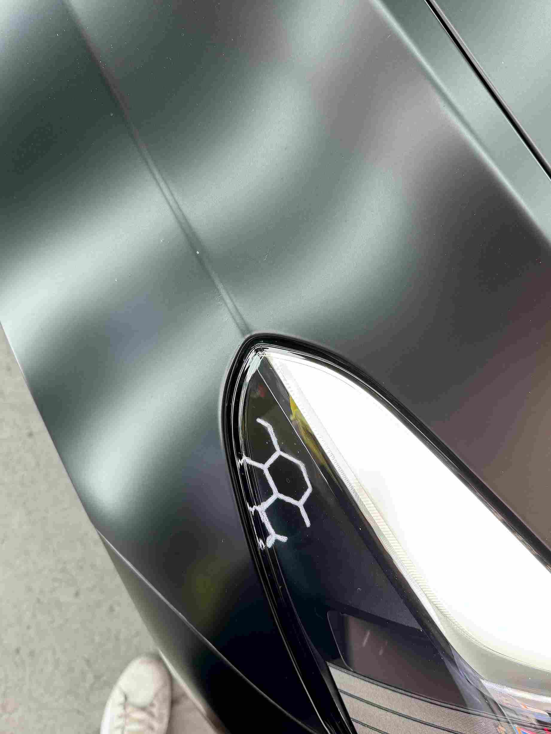 Matte black car hood with a honeycomb design near the headlight.