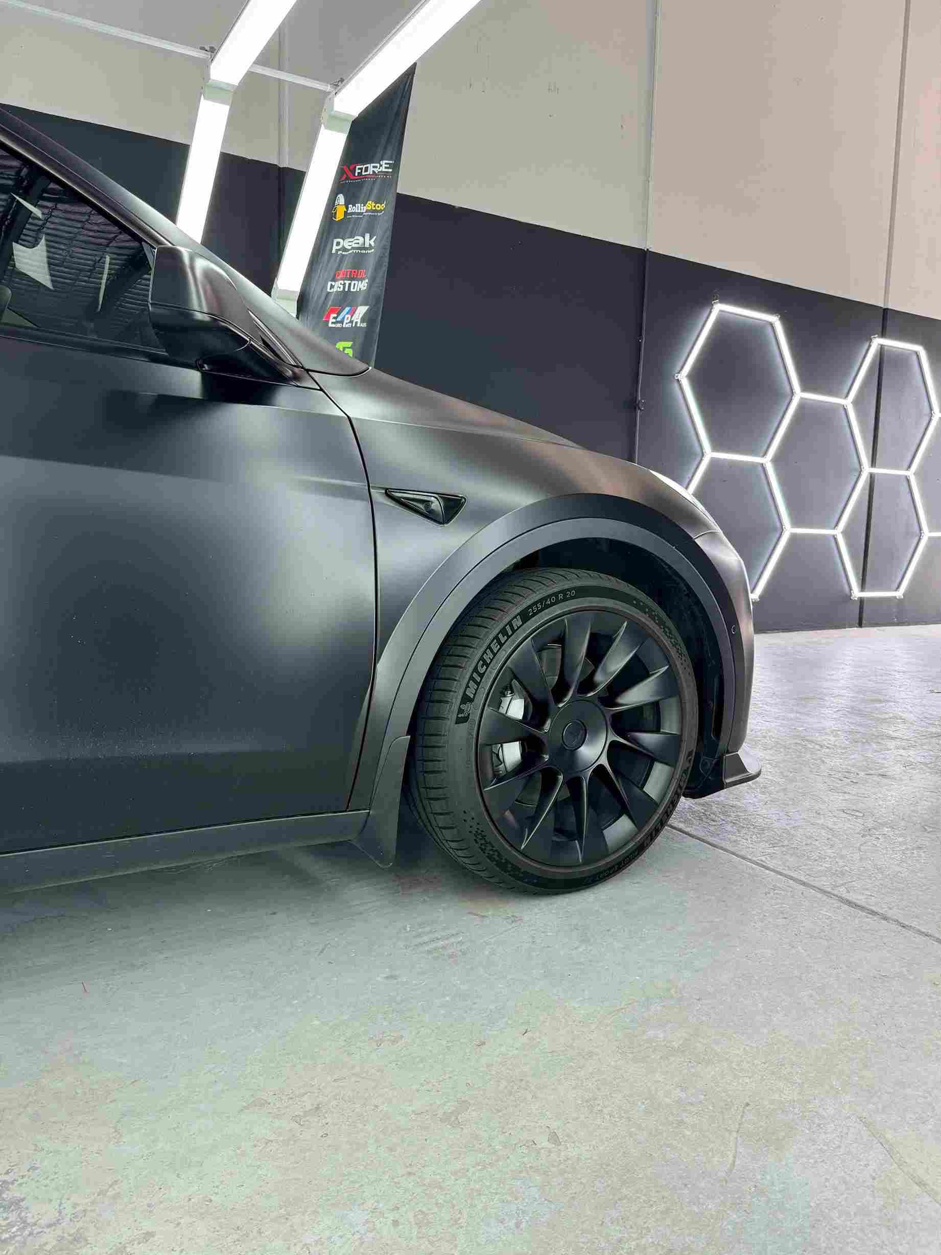 Black Tesla car with black wheels in a garage setting with hexagonal lights.