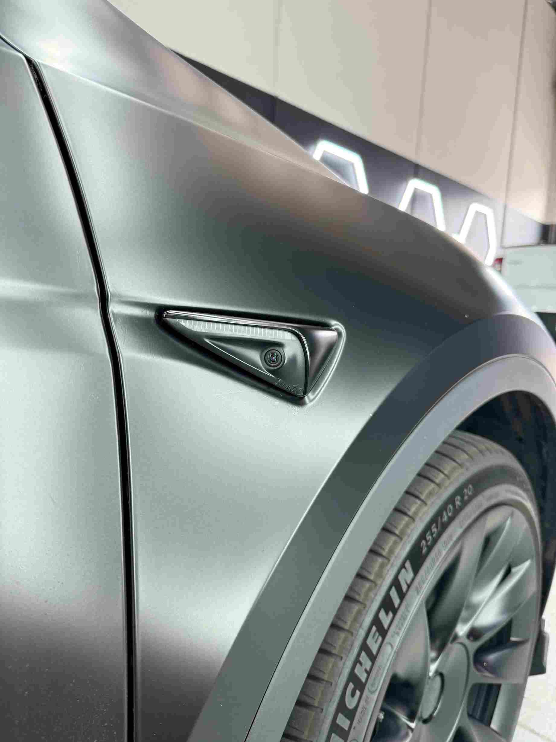 Matte gray Tesla Model X front fender, black emblem, and tire.