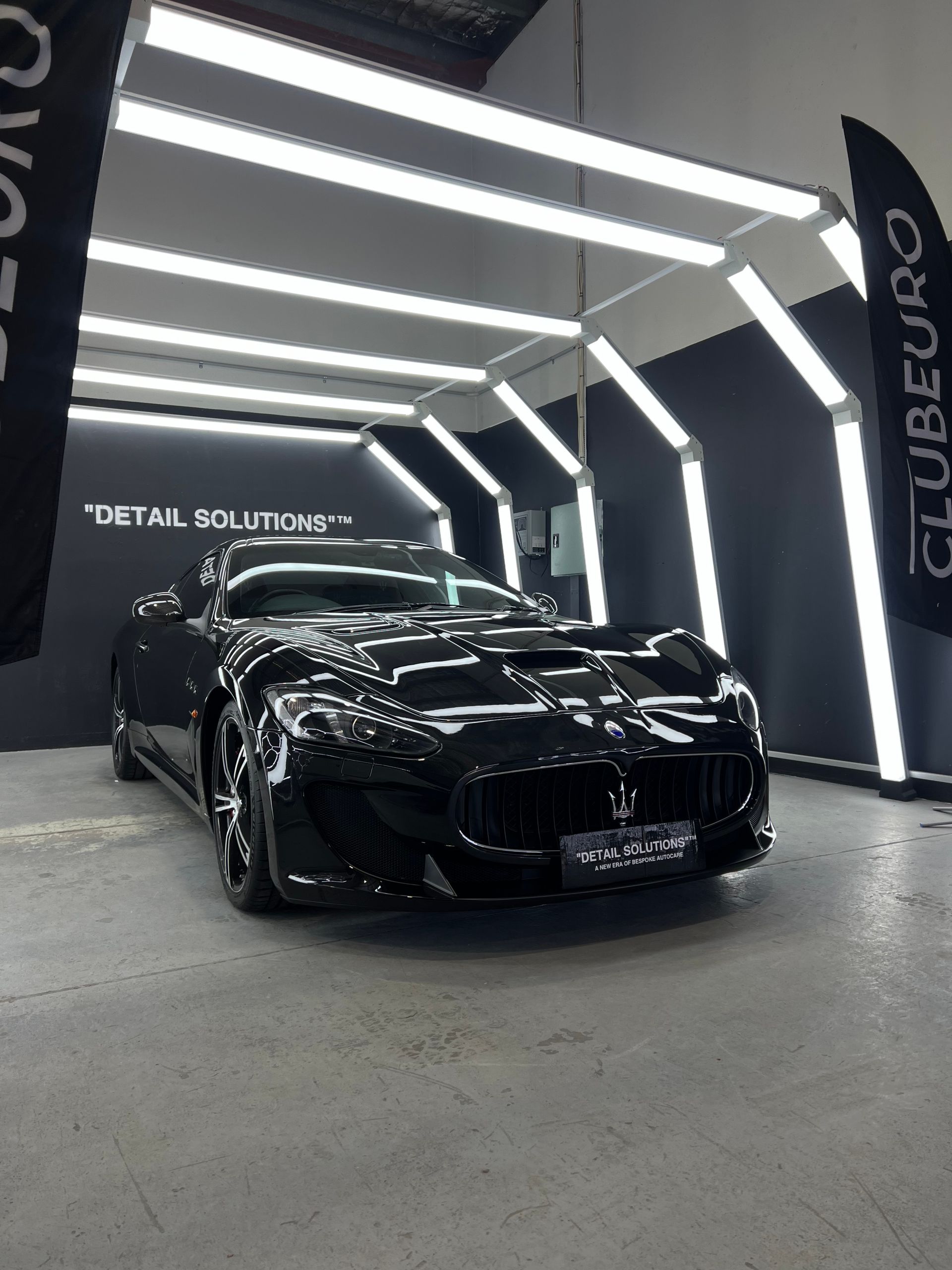 Black sports car inside a detailing shop, illuminated by bright lights.