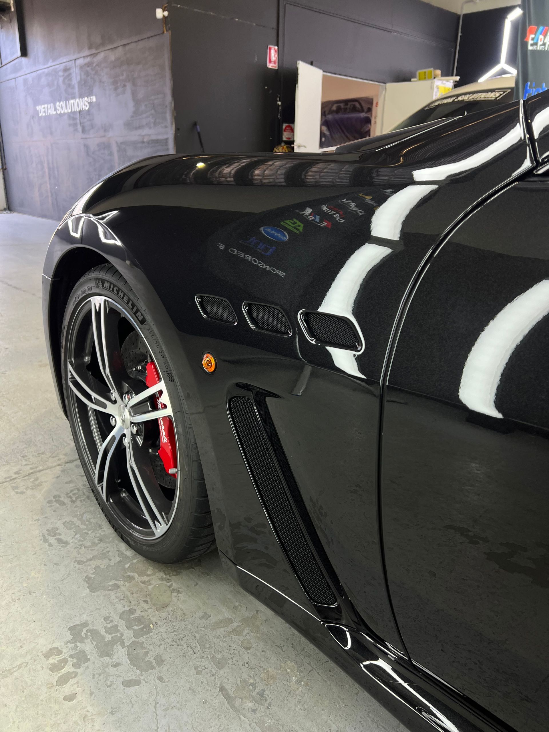Black sports car with red brake calipers and silver rims parked indoors.
