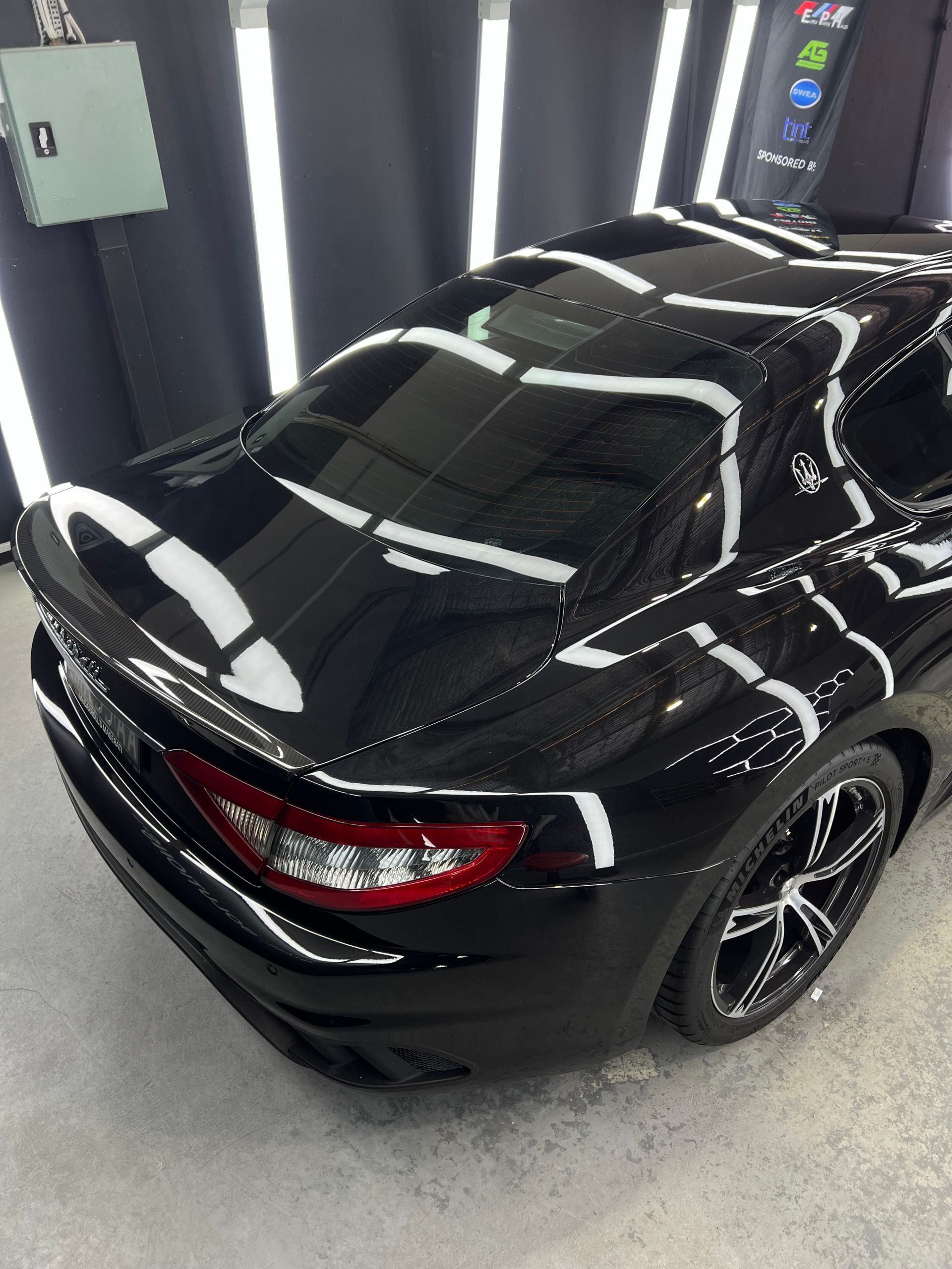 Black Maserati sports car in a brightly lit studio, with reflections highlighting its glossy finish.