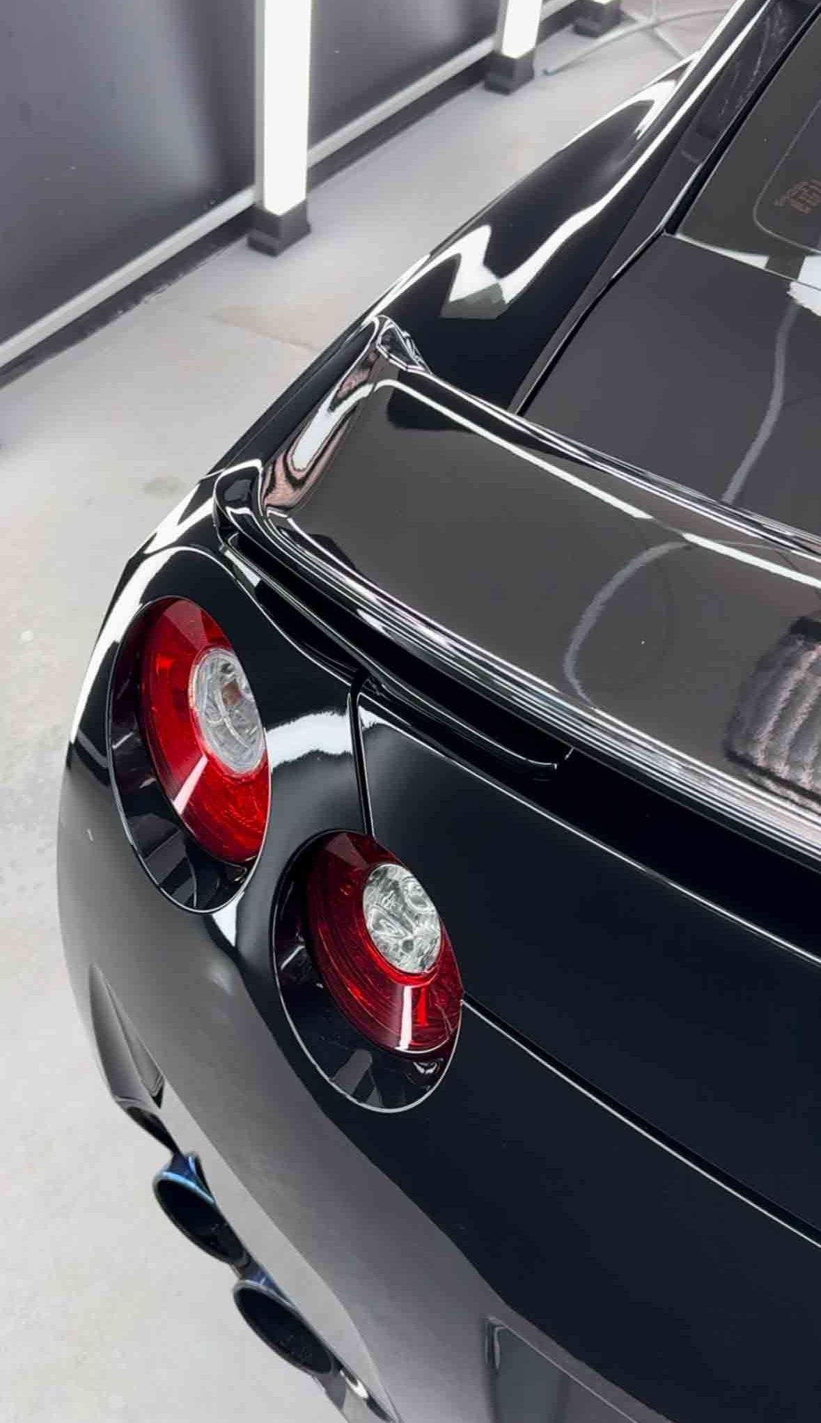 Black Nissan GT-R sports car rear detail, with red taillights and reflective, glossy finish.