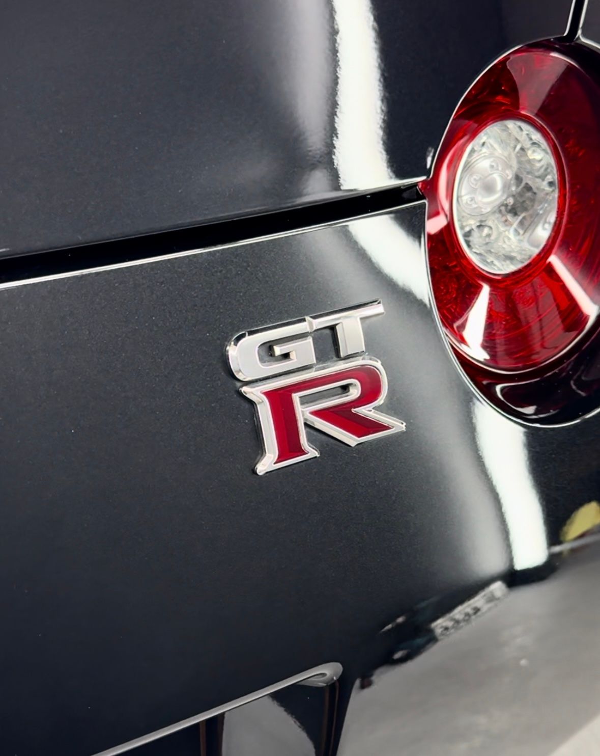 Close-up of a dark grey Nissan GT-R emblem with red accents and a tail light.