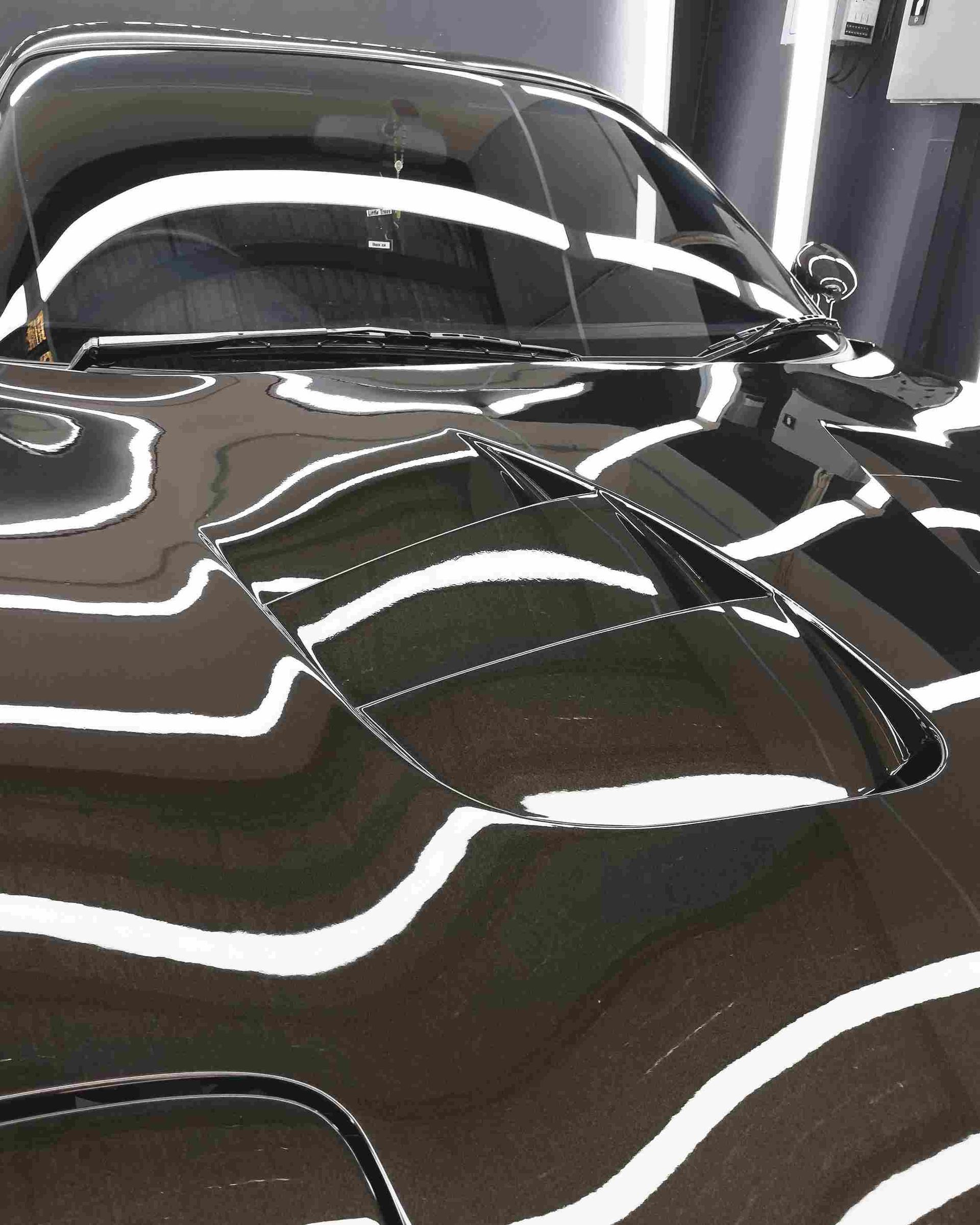 Black sports car hood with reflective white light streaks.
