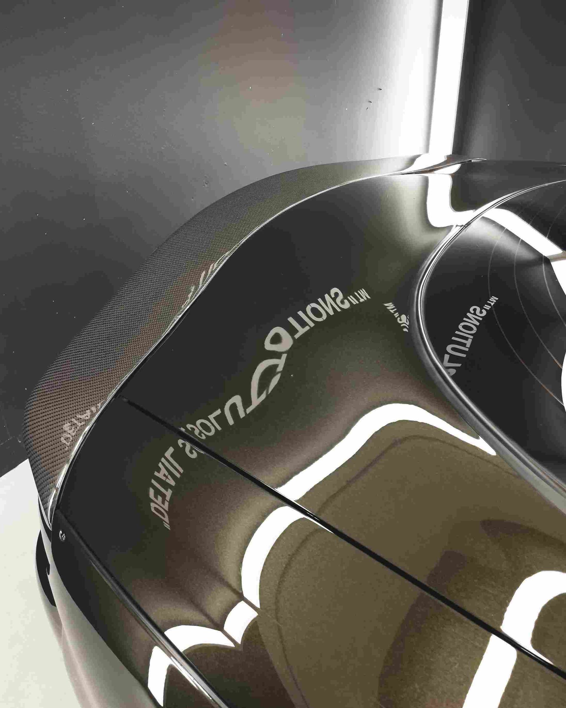 Glossy black curved surface with white lettering and reflections, possibly a car or sculpture.