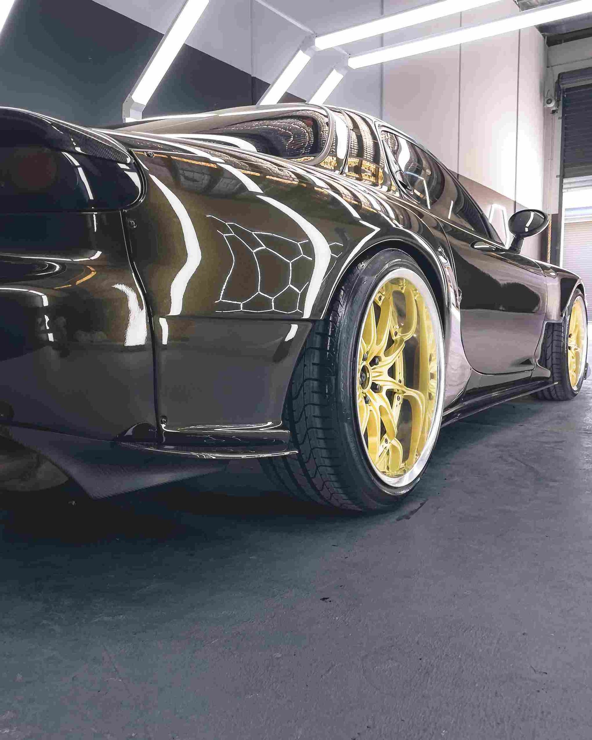 Black sports car with gold wheels, parked inside a brightly lit garage.