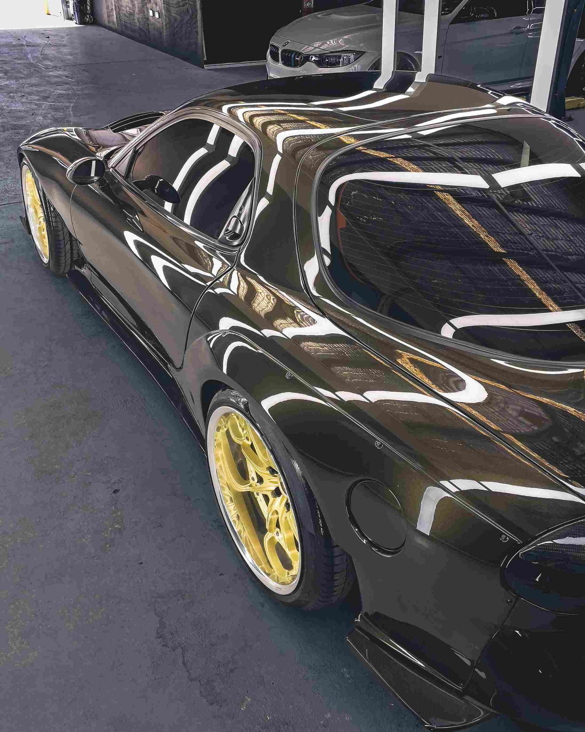 Black sports car with gold rims parked in a garage, reflecting the surroundings.