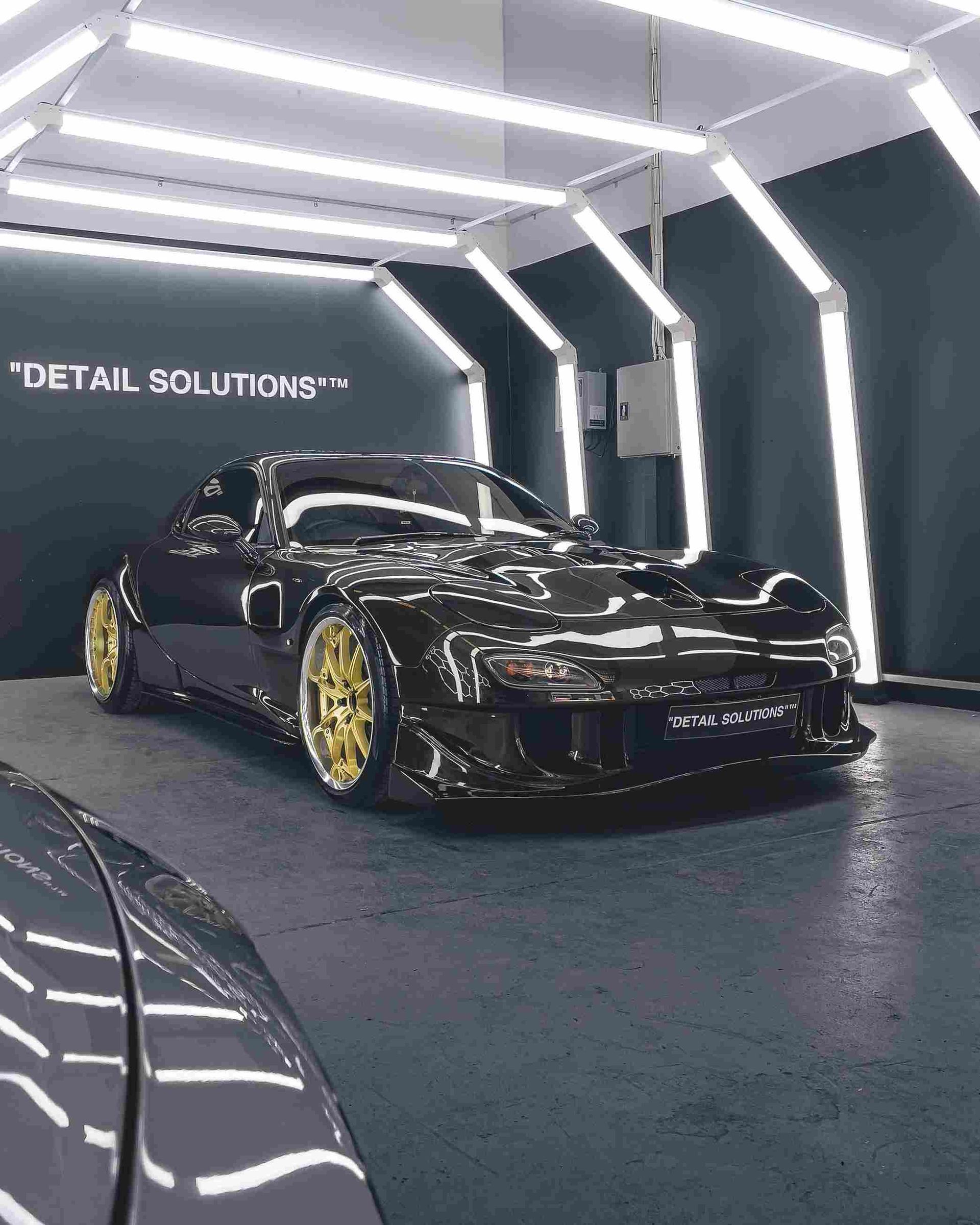 Black custom sports car with gold wheels, in a well-lit detailing shop.