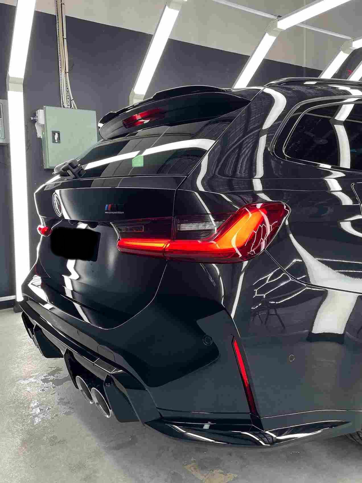 Black BMW station wagon rear with spoiler, taillights, and exhaust in a car wash bay.