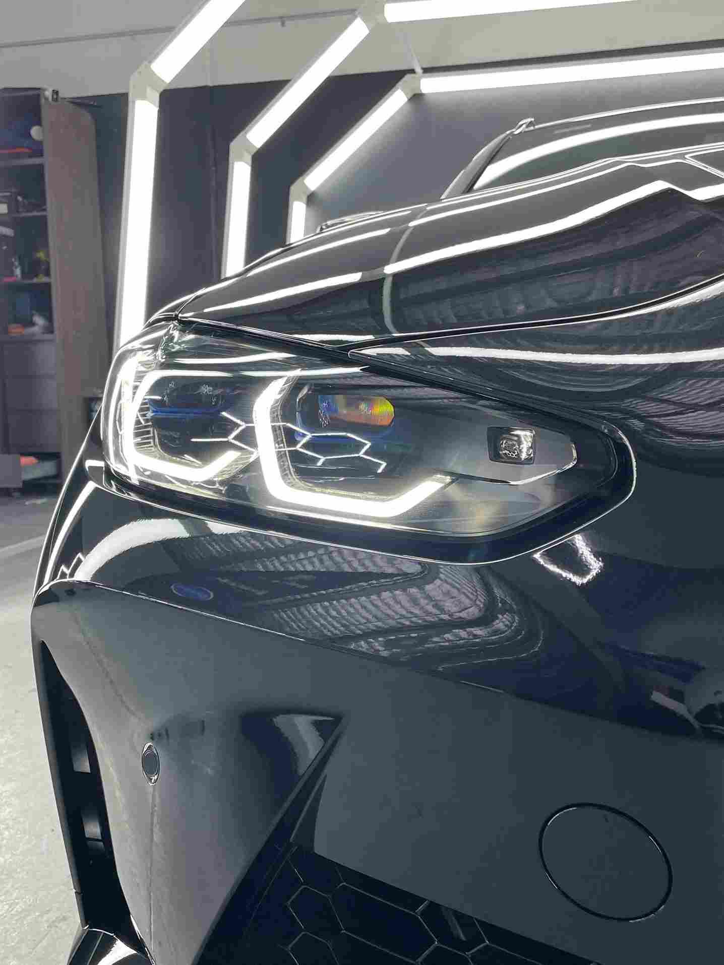 Black car's front with glowing headlights and shiny paint under bright lights.