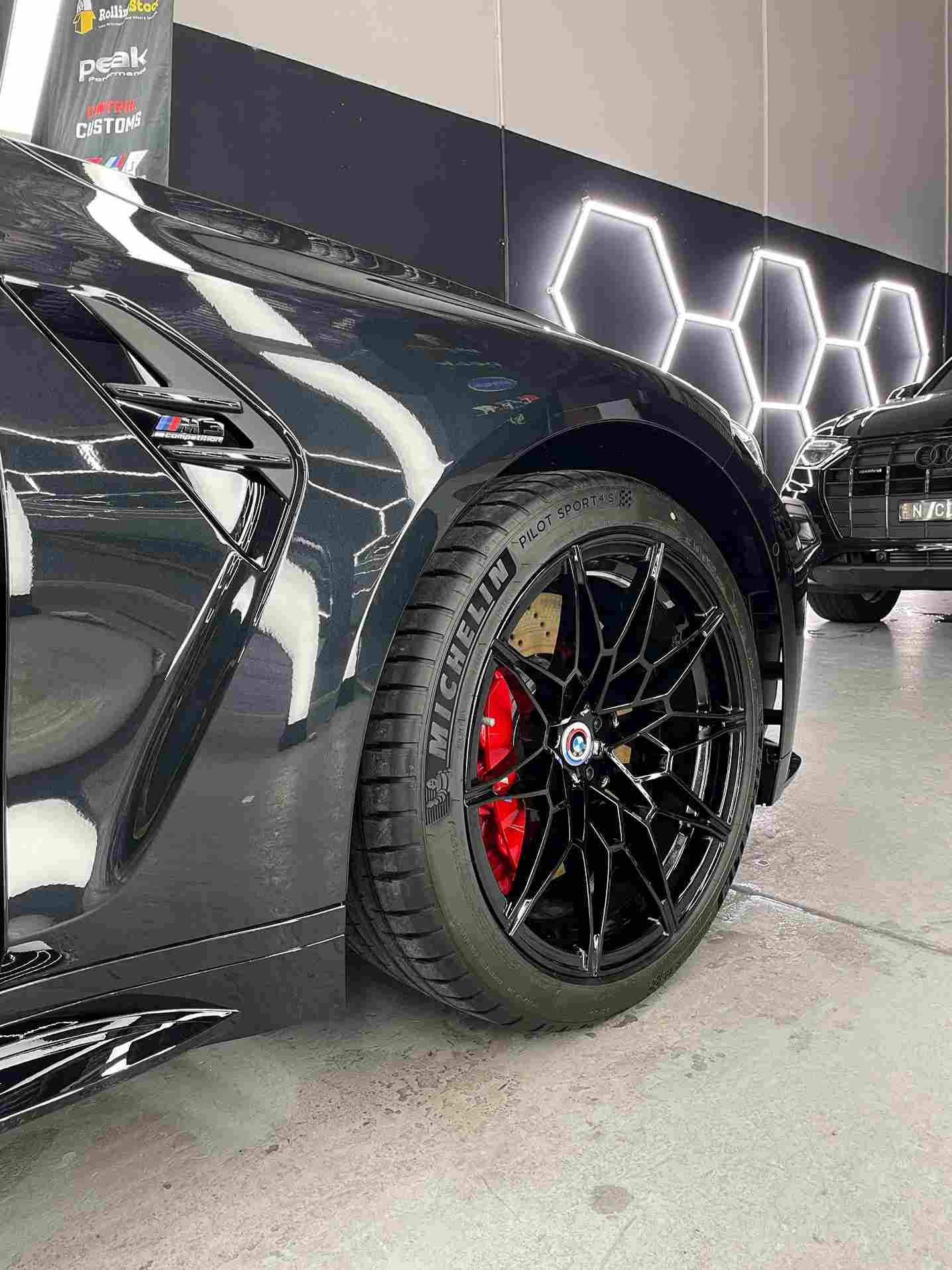 Black car with red brake calipers and black rims parked in a garage with hexagon lights.