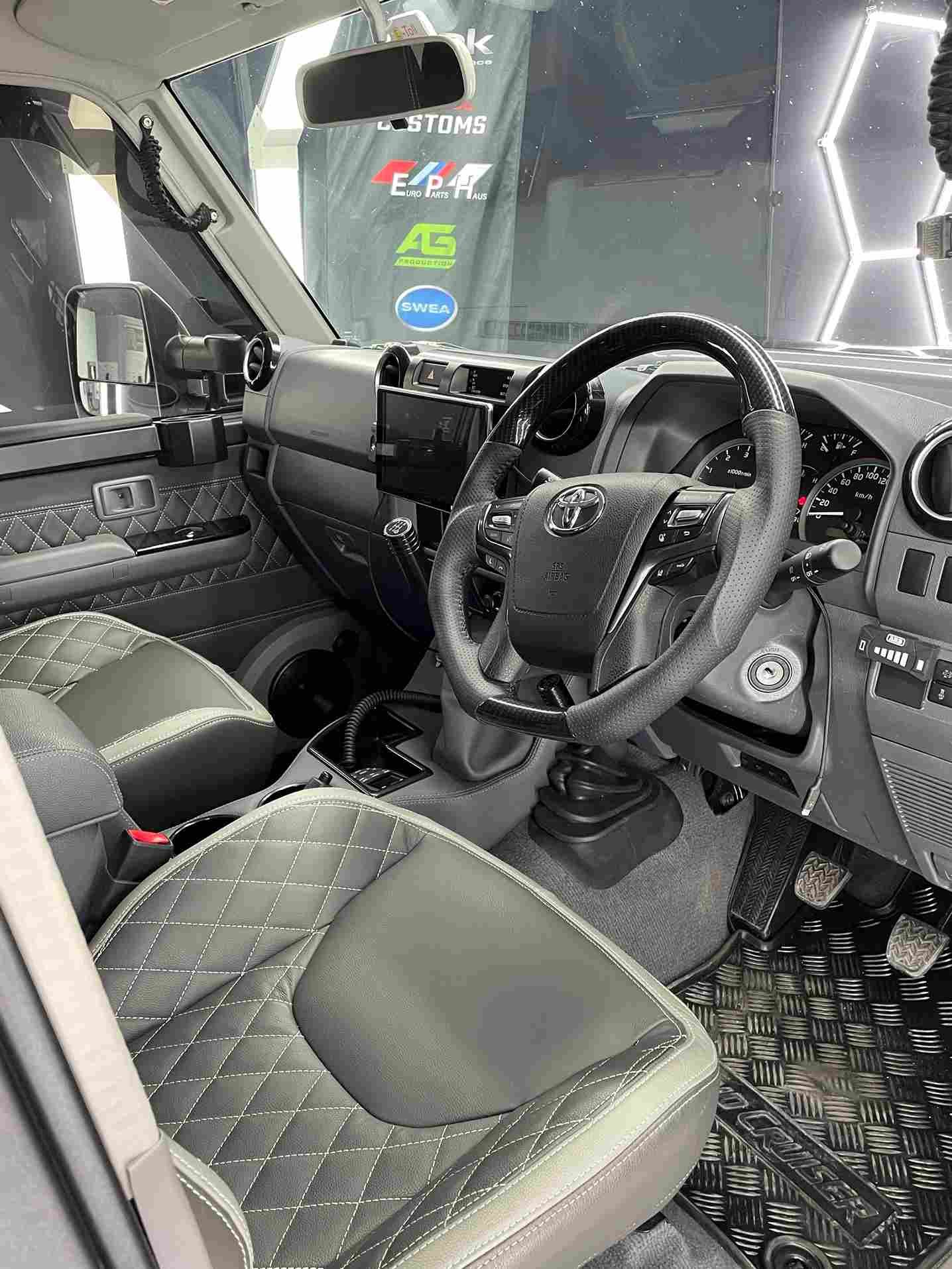 Interior view of a gray and black modified Toyota Land Cruiser. Diamond-stitched seats, metallic floor, and steering wheel visible.