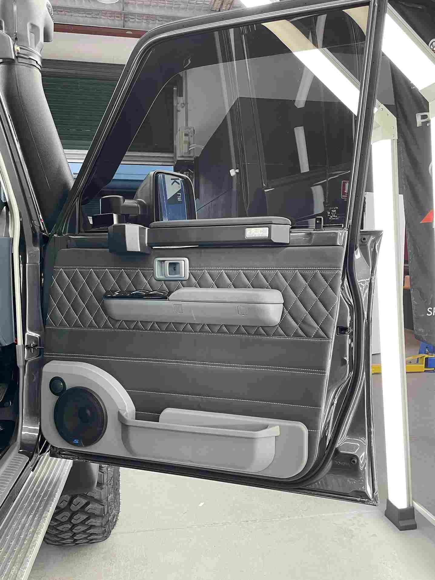 Black car door interior with custom speaker, quilted pattern, and gray door handle.