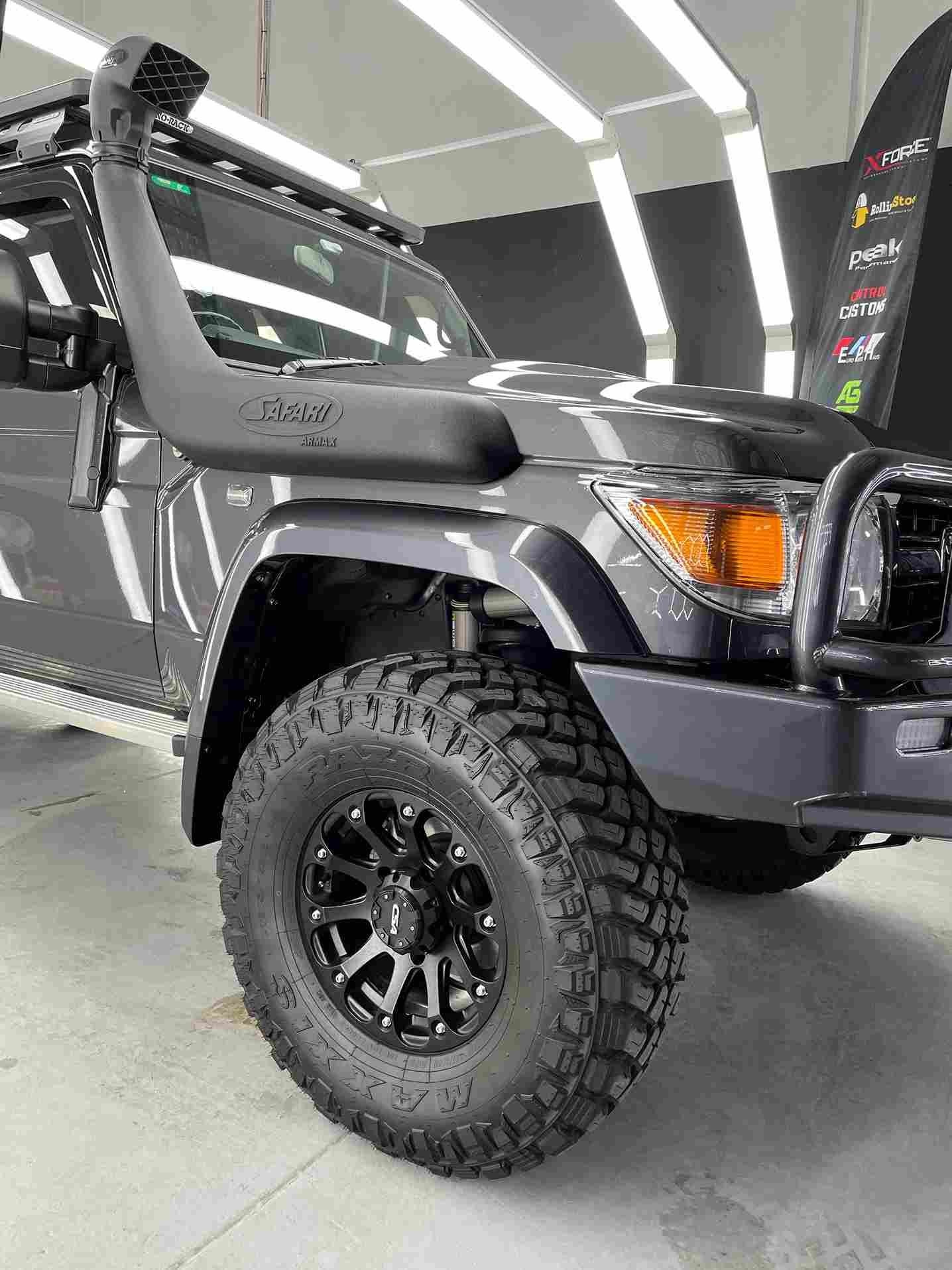 Gray off-road vehicle with large black tires and a snorkel, parked indoors.