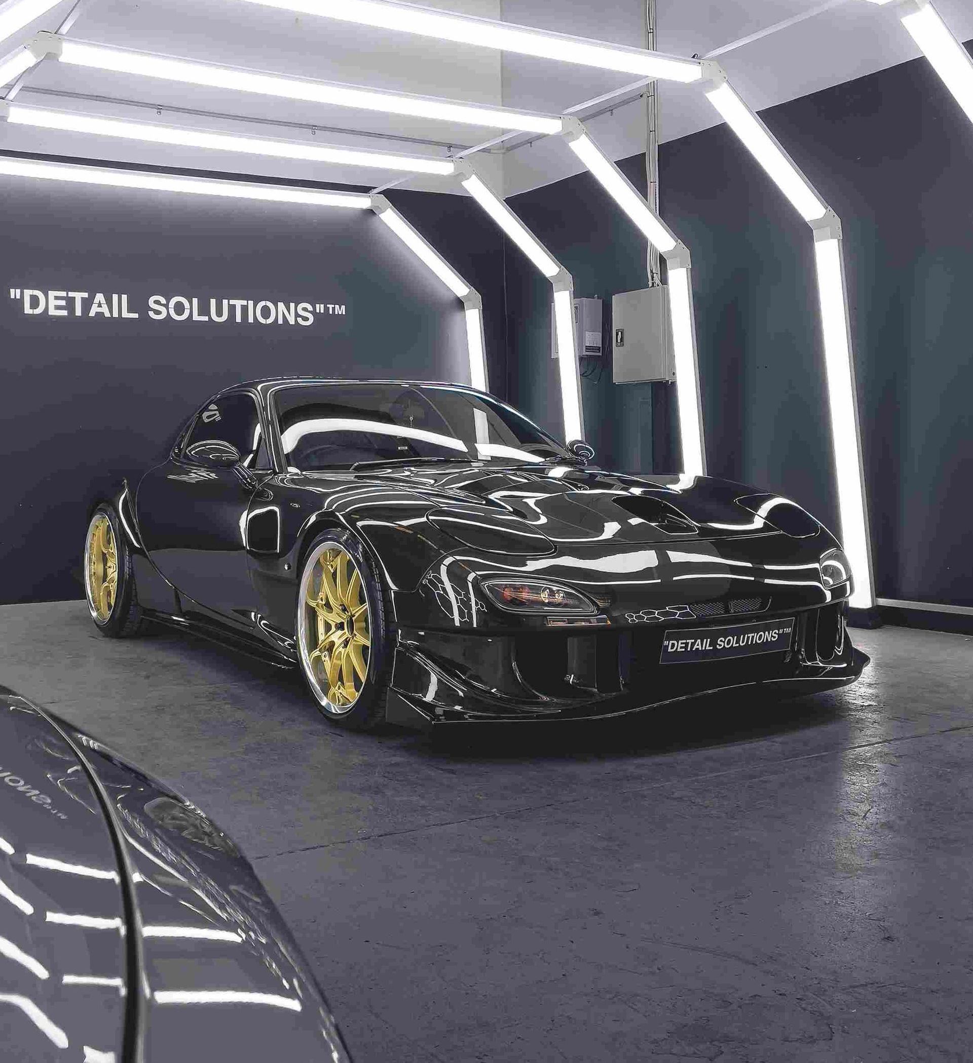 Black sports car with gold wheels in a detailing bay, under bright lights.