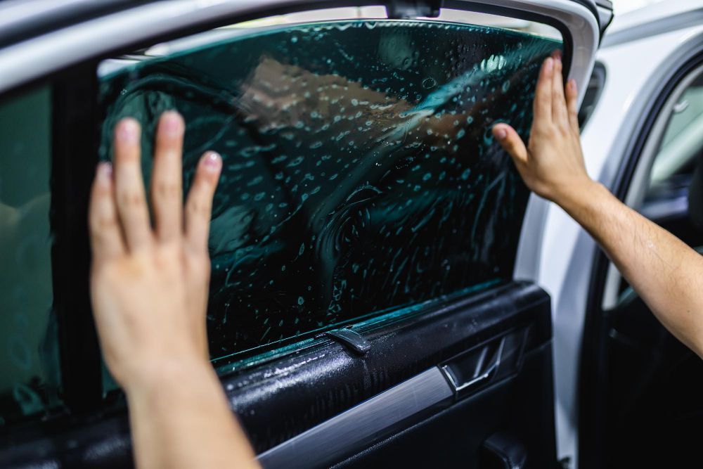 Person applying tinted film to a car window. Hands smoothing out the film, interior car setting.