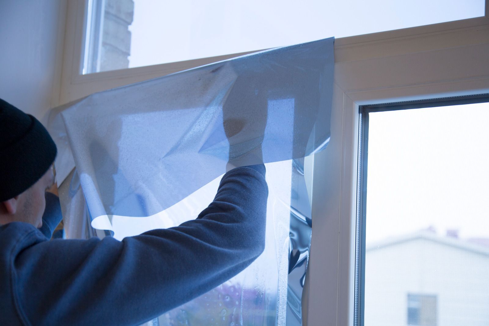 Person applying blue window film to a window in a room.