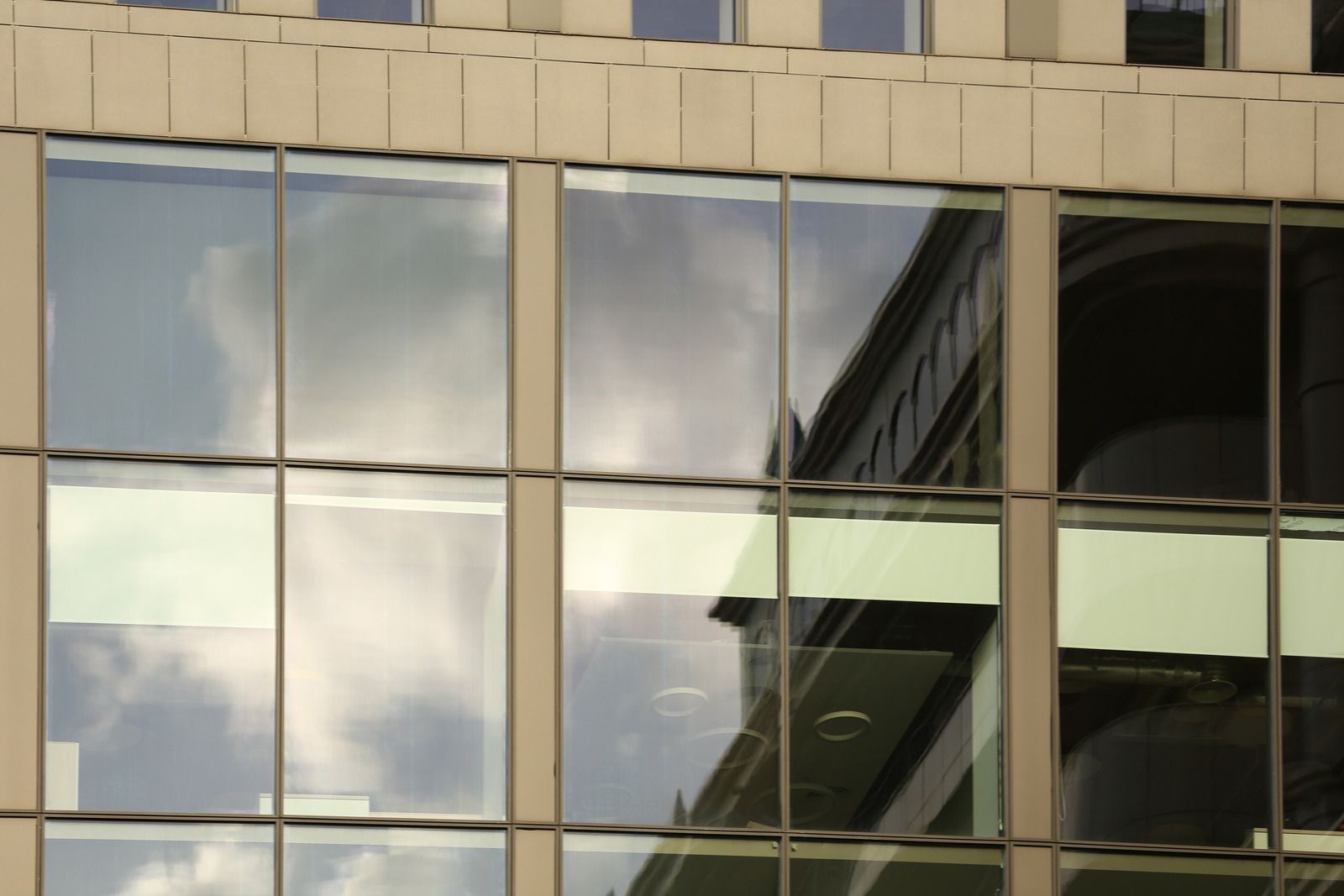 Building facade with reflective glass windows mirroring sky and other buildings.