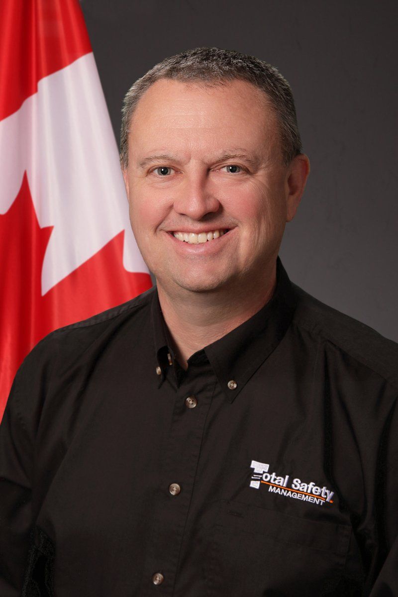 A man in a black shirt is smiling in front of a canadian flag.