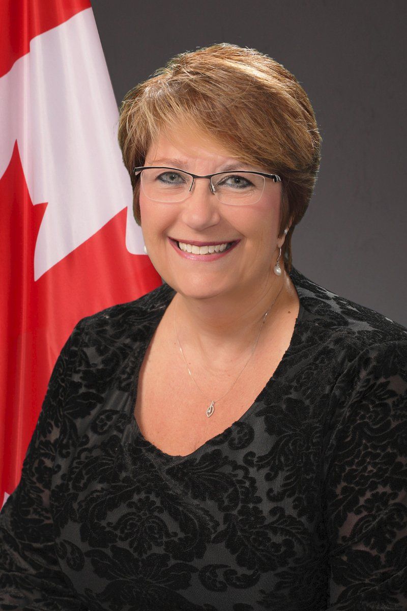 A woman wearing glasses is smiling in front of a canadian flag