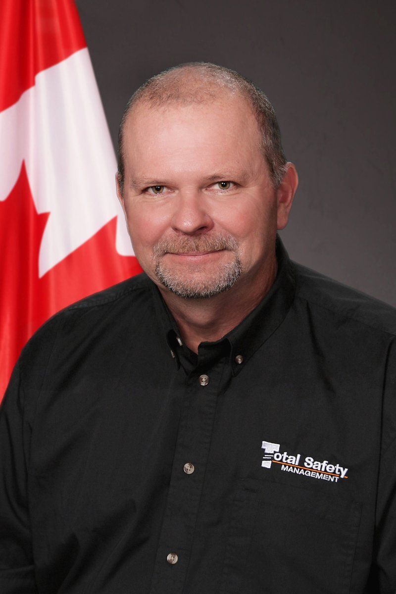 A man wearing a total safety shirt stands in front of a canadian flag
