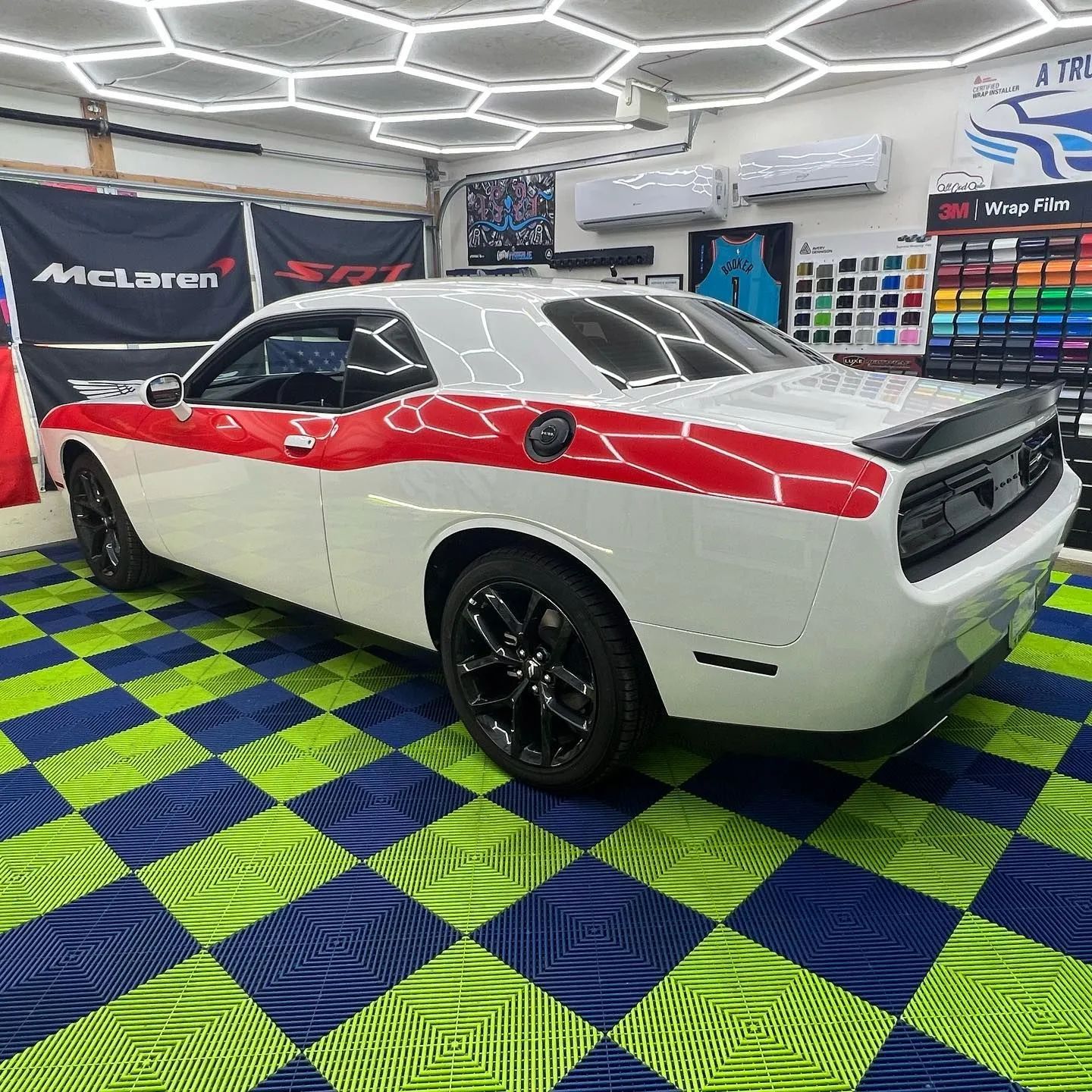 White-and-red Dodge Challenger in a custom wrap shop with colorful tiled floor and wall display.