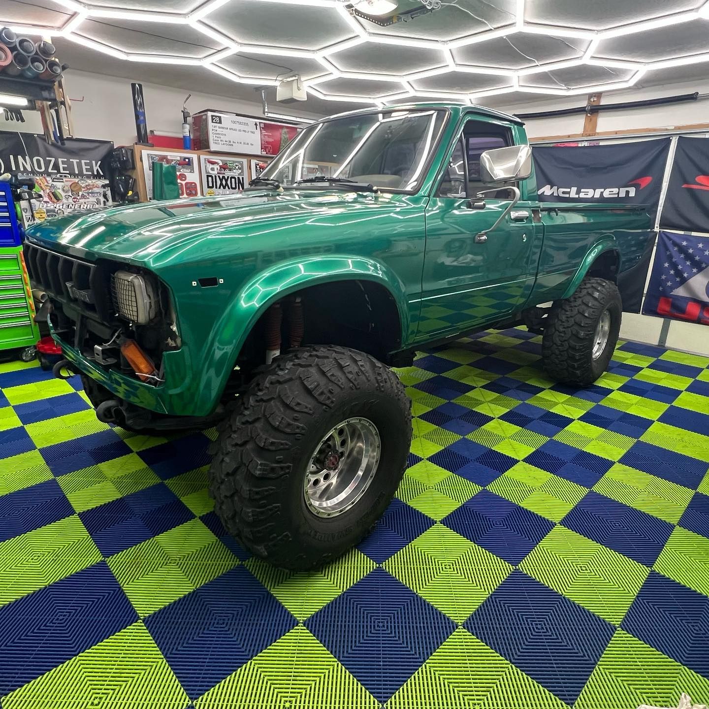 Green Toyota pickup truck with large tires in a garage with a blue and green checkered floor.