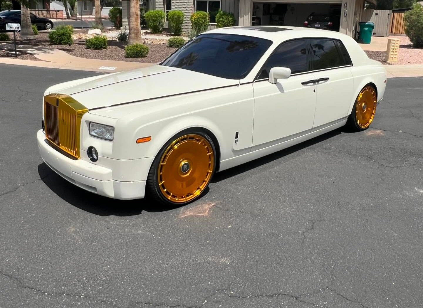 White luxury coupe with gold grille and gold rims parked in a sunlit lot