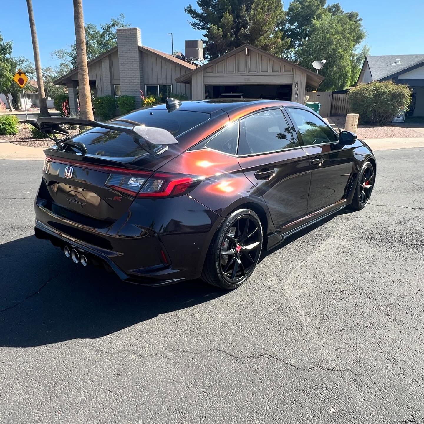 Dark brown Honda Civic hatchback with a large spoiler parked on a sunny street.