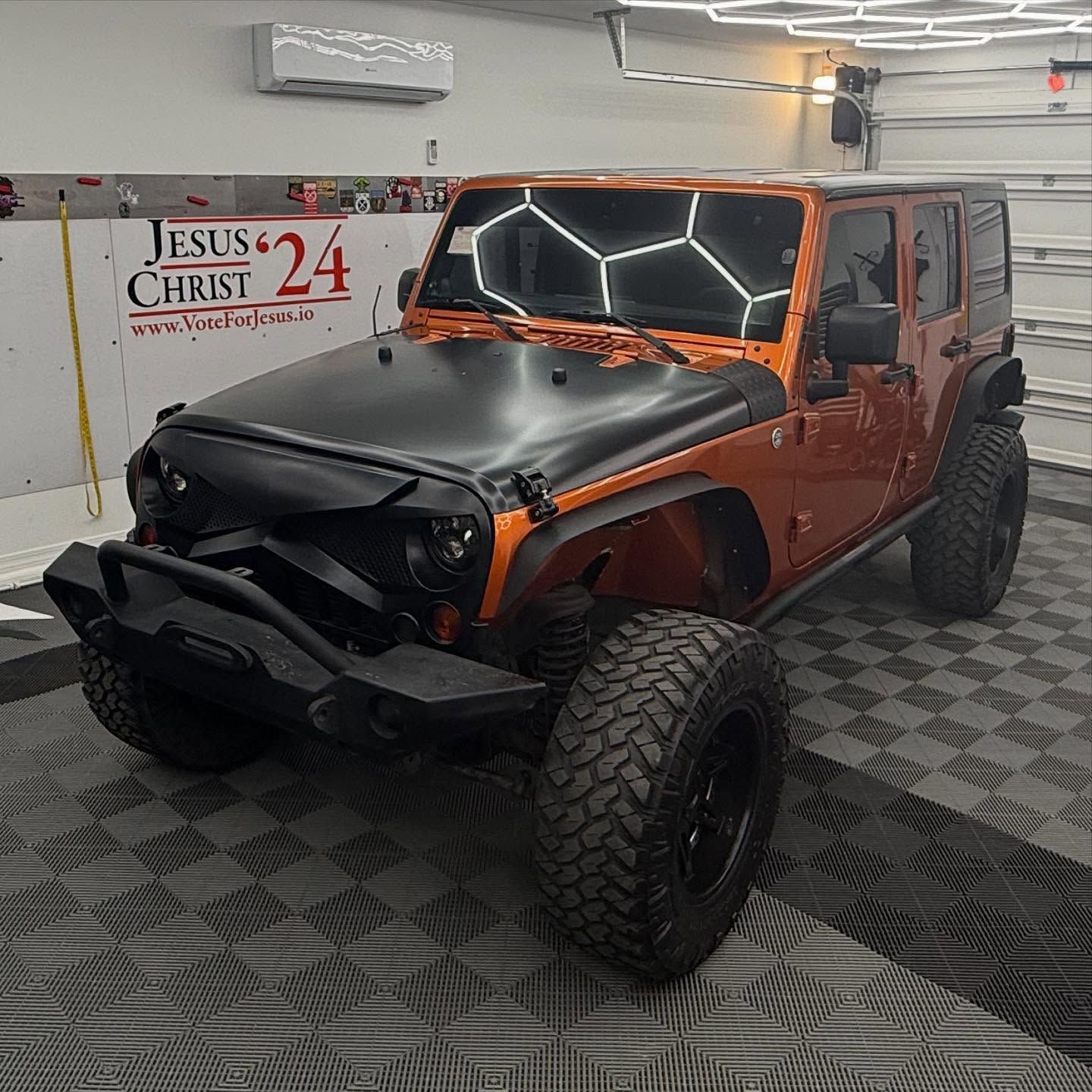 Orange Jeep Wrangler with black accents, inside a well-lit garage.