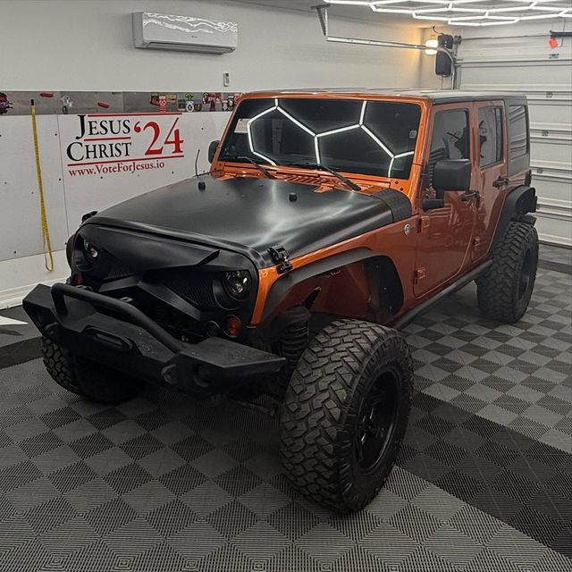 Orange Jeep Wrangler with black hood, bumper, and wheels in a garage.