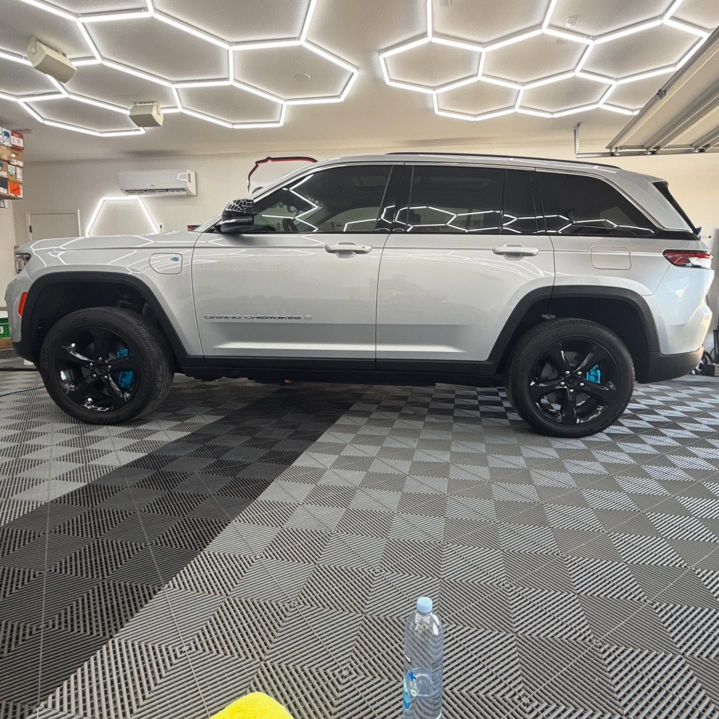 Silver Jeep Grand Cherokee SUV parked in a garage with black and white checkered flooring and blue calipers.