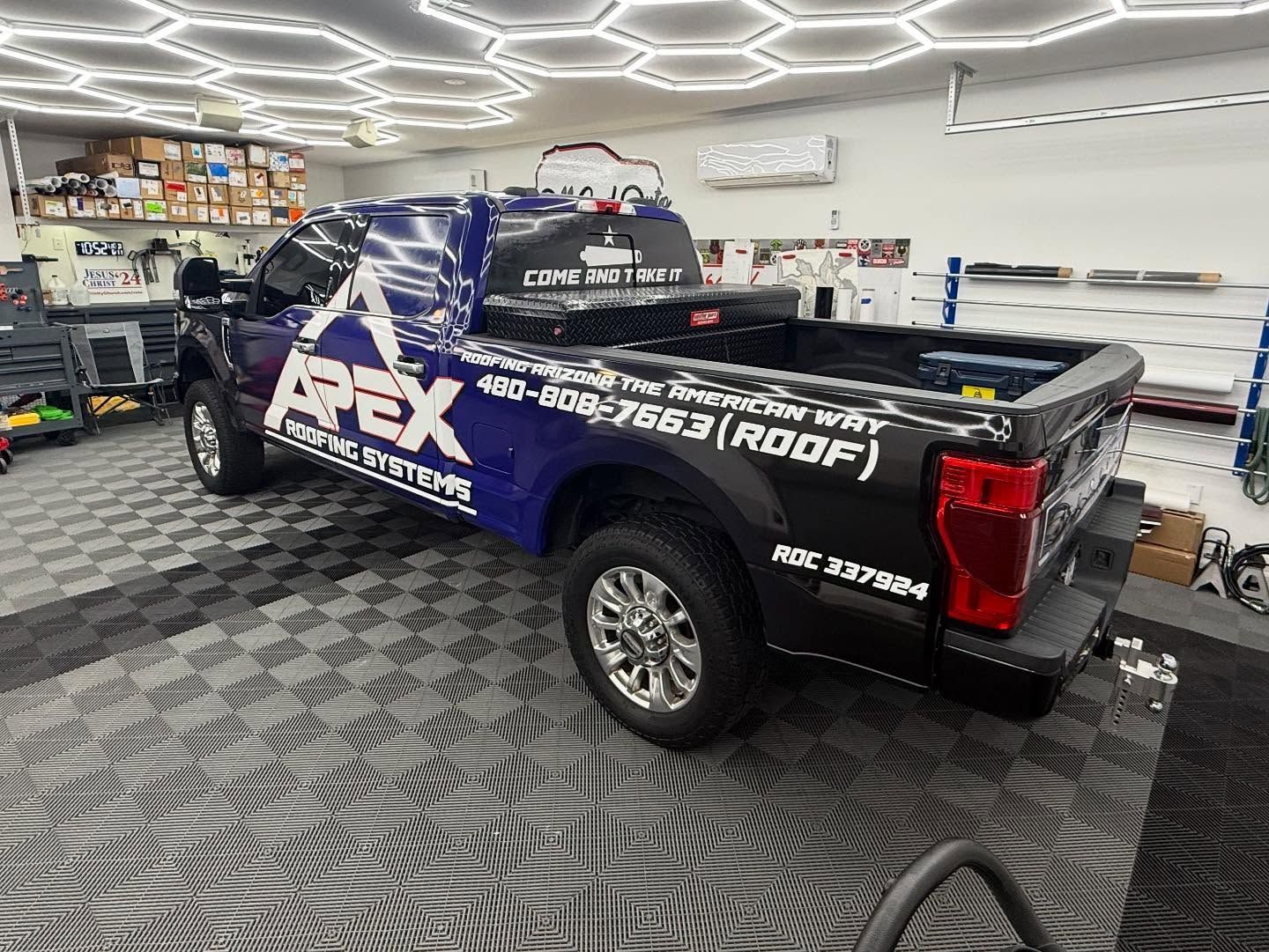 Black and blue Apex truck in a garage, with chrome wheels and company logo on the side.