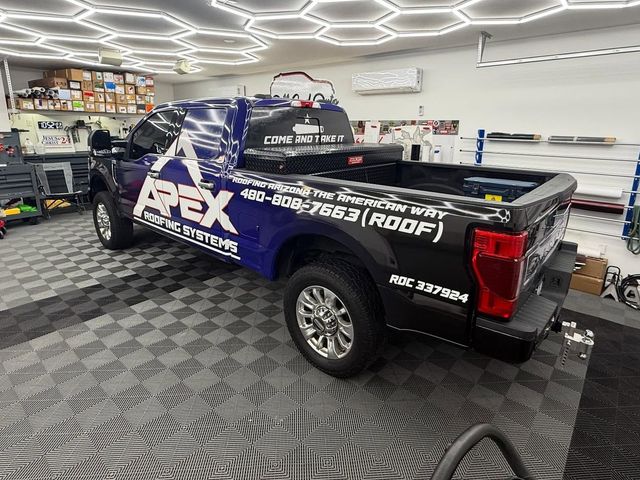 Blue and black Apex Roofing Systems truck in a shop, with the company logo and phone number visible.