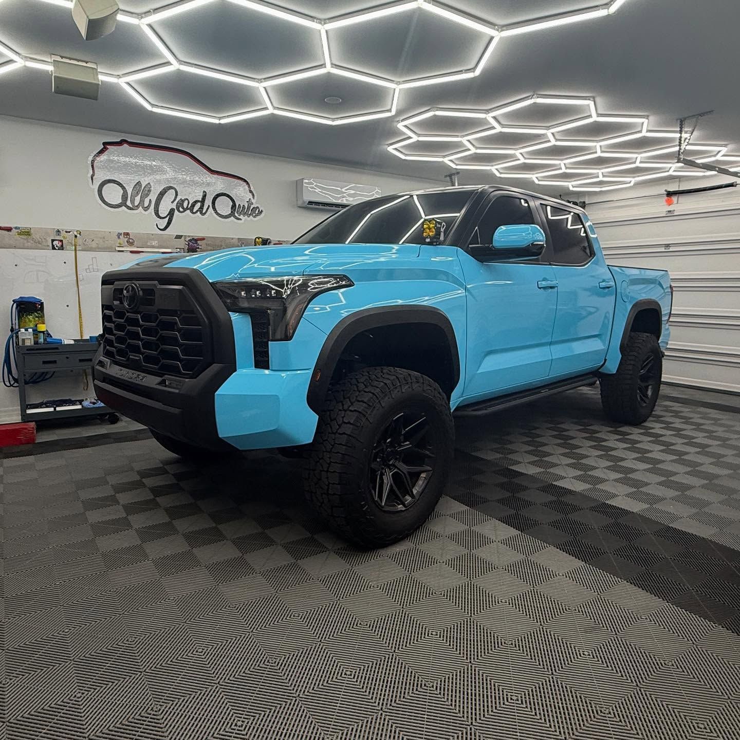 Blue Toyota Tundra truck in a shop. Black grill and wheels. Overhead honeycomb lights.