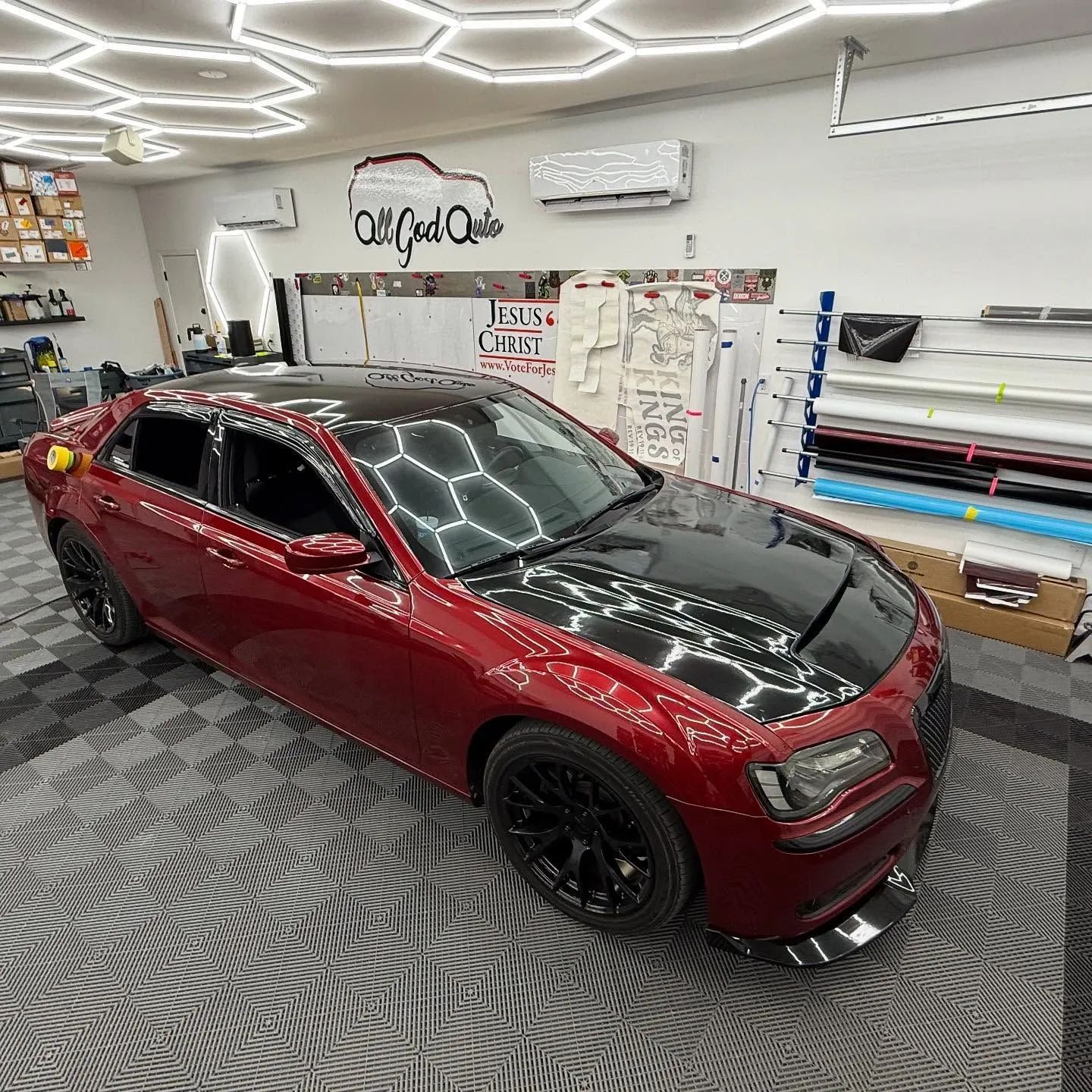 Red sports sedan with black hood in a custom garage with car wraps and detailing supplies