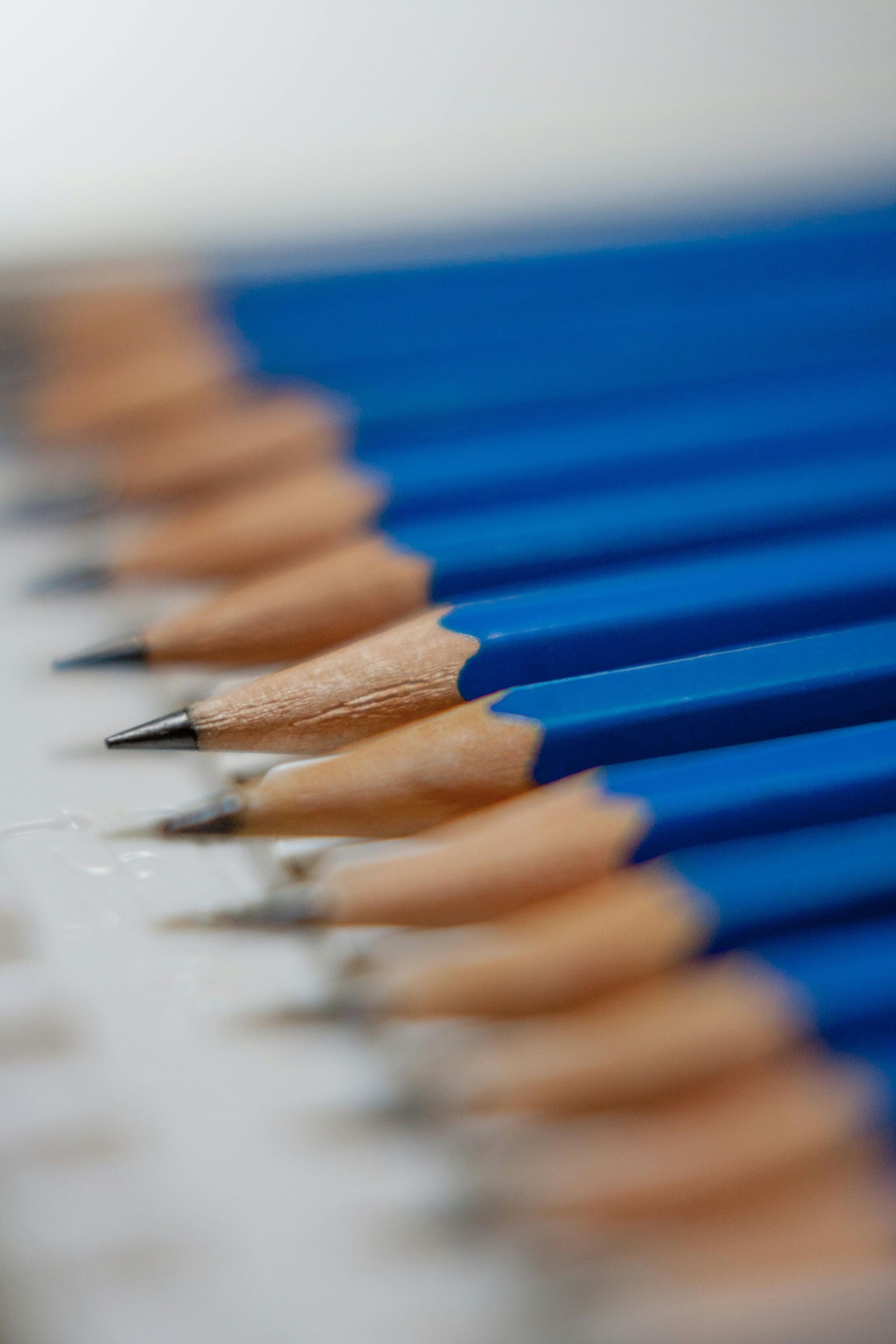 Row of sharpened blue pencils with tan wooden tips, lined up diagonally on a white surface