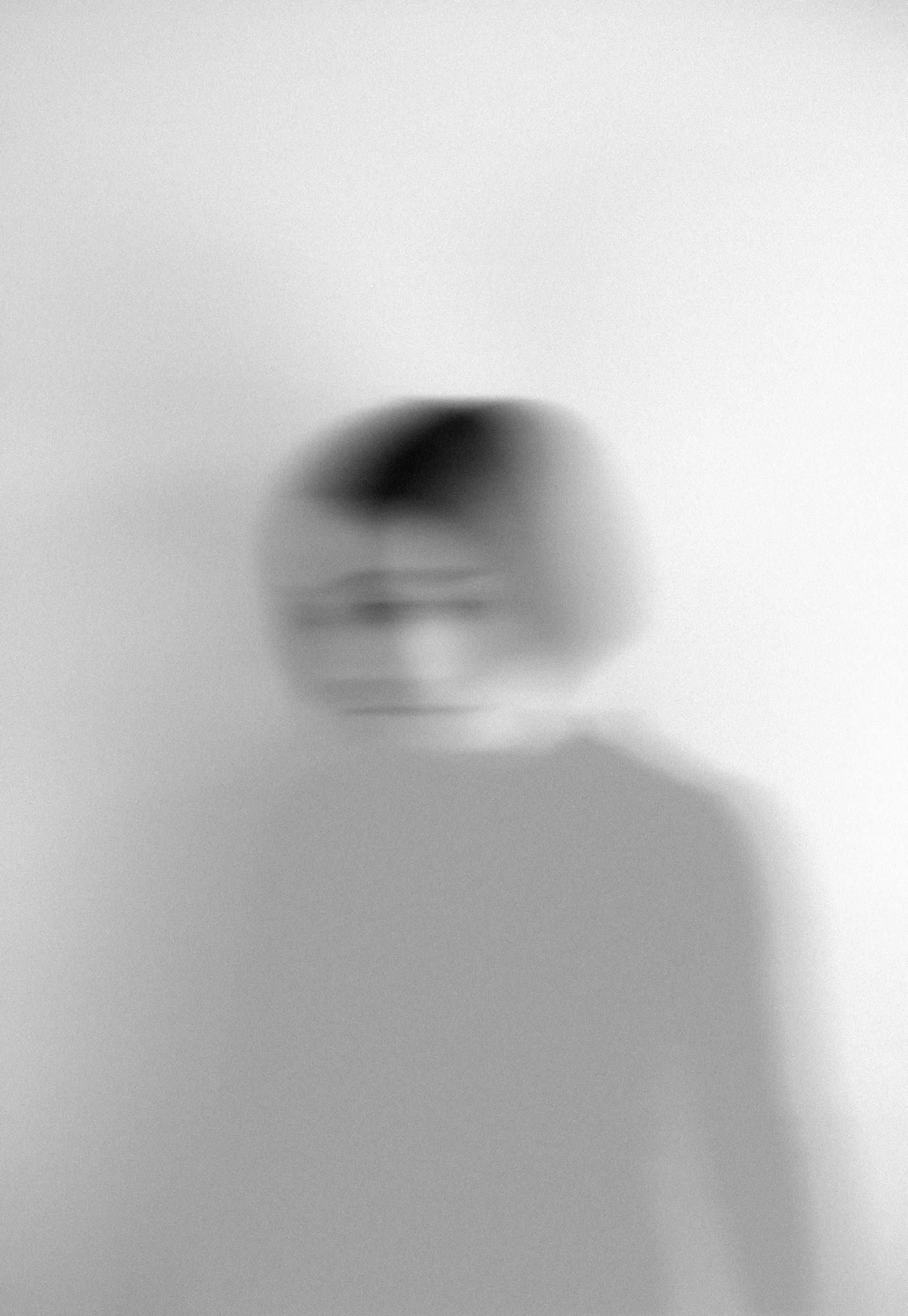 Blurred black-and-white portrait of a person standing against a plain wall