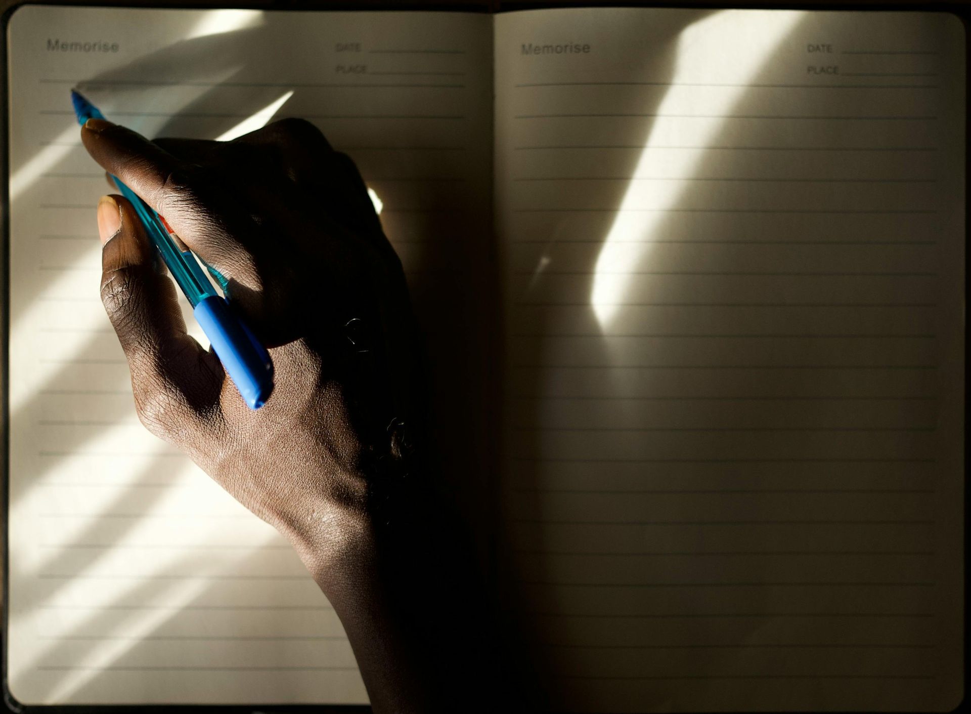 Hand writing in a lined notebook with a blue pen in warm sunlight