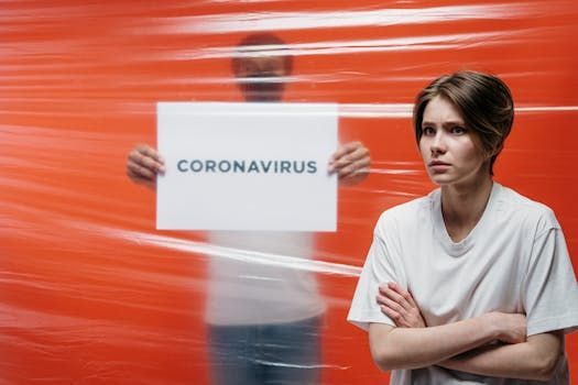 A person stands with arms crossed next to another person behind plastic film holding a sign that says 